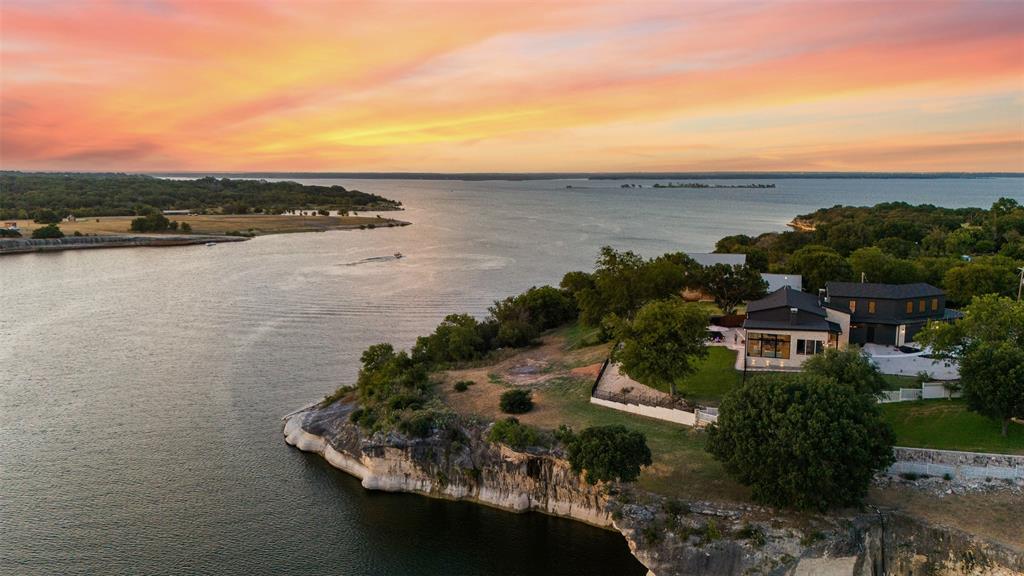 This EXTRAORDINARY lake house, designed and executed by Baker Elite Homes, is a perfect blend of modern sophistication and serene lakeside living, making it a dream home for those seeking both comfort and elegance. You will enjoy 4,430 sqft of luxury living space in the main home overlooking panoramic views of the crystal clear waters of Lake Whitney! Every single room within this home has been intricately designed with high-end finishes that offers comfort as well as functionality within each space. On the interior of the main home you will enjoy having 5 spacious bedrooms, 3 full bathrooms, floor-to-ceiling windows in the main space, a 12-foot kitchen island, fireplaces inside and out, an executive office space, wet bar, 2 large pantries, gym and much, much more. The guest house features 525 sqft with an open-concept, a full bath and is fully furnished. The outdoor space from the gate to the lake is a DREAM and will take your breath..See full description at www.texasluxuryandland.com