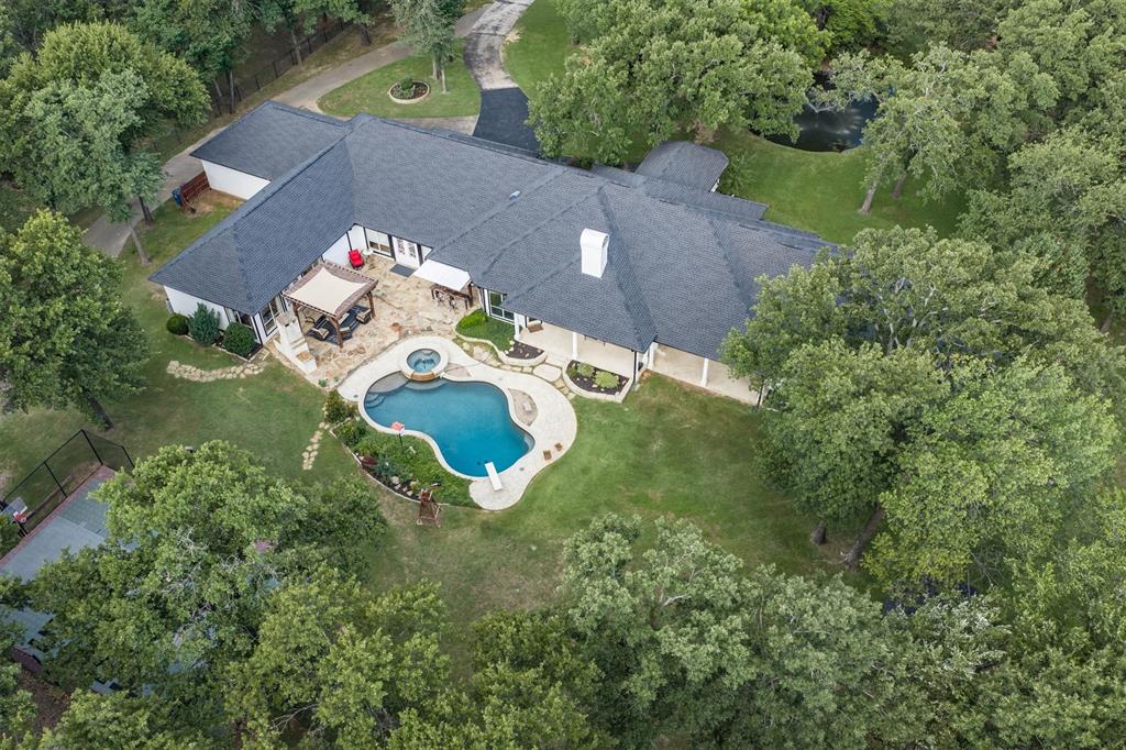 Tucked away at the end of a quiet cul-de-sac in sought-after Canyon Ranch, this gated 6.5-acre Copper Canyon estate offers a rare combination of privacy, recreation, and flexible living spaces surrounded by towering mature trees and natural beauty. Spanning nearly 6,000 square feet, the sprawling single-story residence is designed for both everyday comfort and entertaining, with multiple living areas, hand-scraped hardwood floors, a formal dining room, dedicated office with custom built-ins, media room with theater seating, and a gourmet kitchen featuring custom cabinetry, Viking appliances, double ovens, and dual built-in refrigerators. The primary suite is a private retreat complete with a custom closet and spa-like bath, while a remarkable secondary owner's suite offers approximately 23' x 22' of living space, a wet bar area, and direct access to a large game room, creating an ideal setup for multigenerational living, long-term guests, or private quarters. Step outside and discover a property that feels more like a private park than a residence. Enjoy a sparkling pool, outdoor fireplace, sport court, greenhouse, picturesque pond with fountain, peaceful bridge crossing a seasonal creek, and endless shaded areas to explore beneath the canopy of mature trees. Additional improvements include a guest house with full bath and workshop, a two-stall barn, and a separate accessory building perfect for a craft studio, hobby space, or she shed.Conveniently located just minutes from shopping, dining, and entertainment in Highland Village while maintaining the tranquility and privacy of country living. Zoned to Denton ISD and Guyer High School.