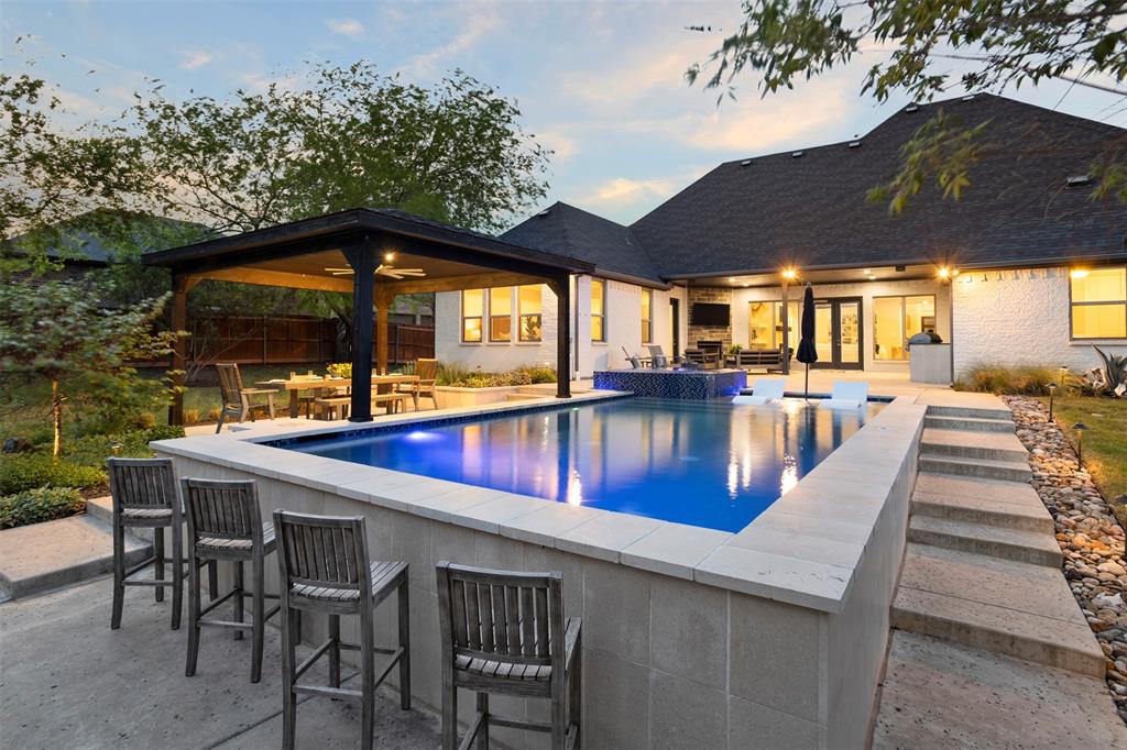 Welcome to a truly custom residence where architectural design, functionality, and luxury living converge in one of North Texas’ most desirable areas. Situated on an expansive ~0.50-acre lot, this 4-bedroom, 3-bath home offers over 3,600 square feet of thoughtfully curated living space with elevated finishes and rare, one-of-a-kind features. From the moment you enter, the home sets itself apart with a custom curved staircase, hand-troweled wall finishes, extensive crown molding, and real hardwood flooring throughout. Oversized windows flood the home with natural light, creating a bright and inviting atmosphere. The open-concept living area connects seamlessly to a chef-inspired kitchen featuring quartz countertops, double ovens, a microwave drawer, built-in wine refrigerator, custom spice storage, and a spacious walk-in pantry. Under-cabinet and display lighting add both function and style. The primary suite on the main level offers a private retreat with vaulted ceilings and a spa-like bath including a soaking tub, walk-in shower with bench seating, dual vanities, and generous storage. The custom closet features built-ins, dresser storage, and a dedicated shoe wall. Additional highlights include a front office with built-ins, oversized secondary bedrooms, a full guest suite downstairs, and an upstairs media room with a 100-inch screen, 4K projector, and surround sound. Step outside to a resort-style backyard with a covered patio, fireplace, built-in audio, and outdoor kitchen with grill and Green Egg. The custom pool and spa feature an infinity-edge hot tub, volleyball layout, seating ledges, and upgraded equipment with WiFi connectivity. The deep, tiered lot provides added privacy and space. Additional features include a 3-car garage with EV Level 2 charger, smart thermostats, dual HVAC systems, built-in storage, and whole-home audio wiring. Located near 287, 35W, and the greater DFW area, this home offers a rare blend of privacy, luxury, and accessibility.