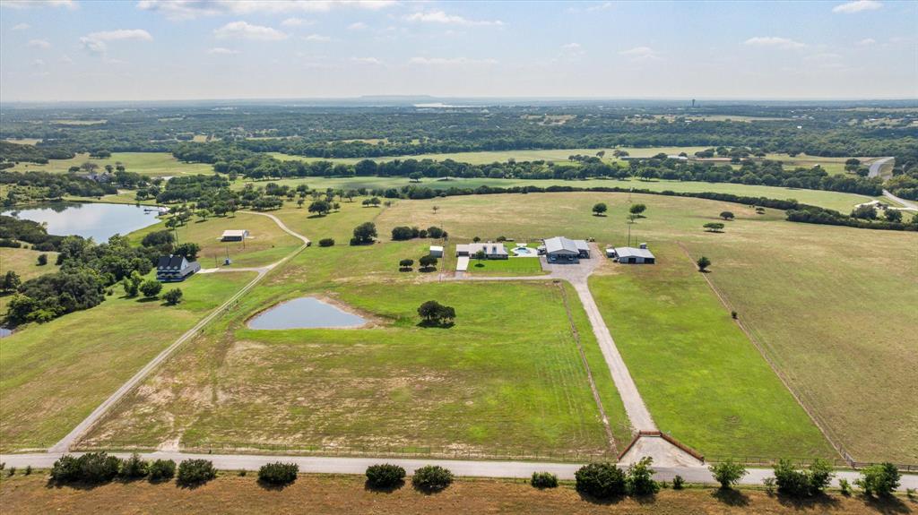 Experience the perfect blend of luxury, functionality, and wide-open Texas living at this stunning ranch estate. Situated on beautifully maintained acreage with panoramic countryside views, this exceptional property is designed for those who appreciate both elegant living and practical ranch amenities. The beautifully appointed home features timeless stone construction, a durable metal roof, expansive covered porches, and picturesque views from every direction. The resort-style backyard is an entertainer’s dream, complete with a custom in-ground pool, raised spa, spacious tanning ledge, and an inviting outdoor living area perfect for relaxing or hosting family and friends. The 50'X65' insulated shop complete with a CMU concrete safe room and office space has 14' sidewalls and 12' door openings, offers endless possibilities with abundant workspace, covered RV and equipment parking, and room for all your hobbies, business operations, or recreational vehicles. The property also includes horse stalls, loafing sheds, additional outbuildings, cross-fencing, a seasonal stock pond, and lush pastures ideal for horses, livestock, or simply enjoying the peace and privacy of country living. The gated entrance and long private driveway create an impressive arrival while maintaining privacy and security. Conveniently located just minutes from Granbury with easy access to Fort Worth, this rare property offers the best of rural living without sacrificing modern conveniences. A few property highlights include a beautiful custom ranch home with metal roof, resort-style pool and spa, outdoor cooking and entertaining area, large insulated shop with covered parking, gated entrance with long private drive, seasonal stock pond and improved pasture, horse stalls, fenced and cross-fenced acreage, and breathtaking panoramic Texas views. This is more than a home—it’s a lifestyle where luxury meets the Texas countryside.