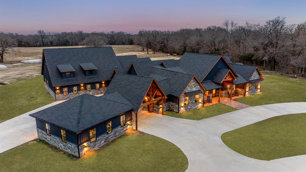 Completed in 2023, this expansive 7,265-square-foot single-story residence combines sleek modern design with classic ranch-style architecture. The home’s exterior is clad in natural stone and wood siding, exuding rustic elegance, while the interior features soaring ceilings, custom finishes, and an open floor plan that enhances the sense of space. Large, panoramic windows throughout the home invite natural light and showcase breathtaking views of the property’s rolling hills and pastures.
The five spacious bedrooms and seven bathrooms offer luxurious comfort, with the master suite boasting a spa-like en-suite bath and private access to the outdoor living area. The gourmet kitchen is perfect for entertaining, equipped with high-end appliances, a large center island, and custom cabinetry. A home theater, game room, and outdoor living spaces, including a resort-style pool, complete the home, providing endless opportunities for relaxation and recreation.
The recently completed guest house provides an additional 1,260 square feet of elegant living space, ensuring guests experience the same level of comfort and sophistication.
At the heart of this estate is a 9,600-square-foot modern barn, built in 2023, featuring stables, paddocks, and equestrian facilities designed for professional and recreational use. The ranch also includes well-maintained fencing, rolling pastures, and multiple stocked ponds, ideal for cattle or equestrian activities. With abundant space for trail riding, fishing, and outdoor adventures, the property offers an idyllic setting for those seeking an active, outdoor lifestyle.