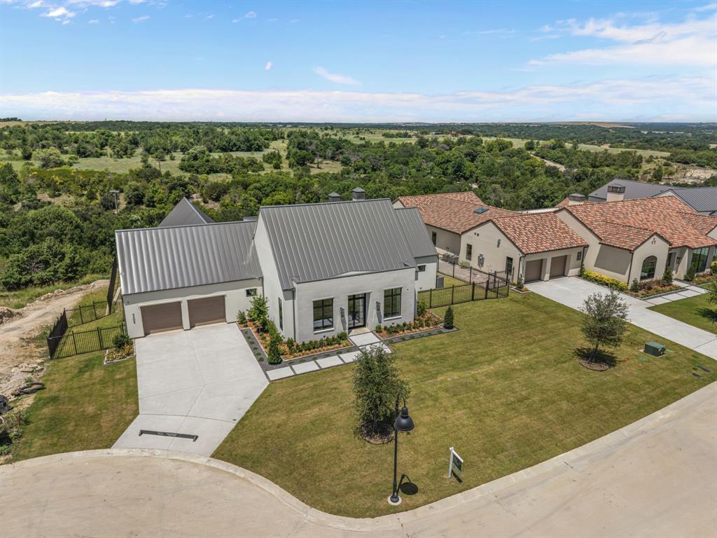 Exquisite new construction by Olerio Homes in Montrachet, one of Fort Worth’s premier gated and 24-hour guarded communities. Offering 4 bedrooms, 4.5 baths, and 4,753 square feet, this thoughtfully designed residence blends refined architecture, elevated finishes, and a highly livable floor plan. A striking exterior with clean lines, a metal roof, and timeless stone accents sets the tone, while steel-and-glass doors open to a light-filled interior with wide-plank hardwood floors, tall ceilings, designer lighting, and beautiful architectural detail throughout. The main level is designed for both everyday living and entertaining, featuring a formal living or study, an open-concept family room with beamed ceilings, fireplace, custom built-ins, and seamless flow to the dining area and chef’s kitchen. The kitchen offers a large center island, commercial-style appliances, extensive cabinetry, and a nearby wet bar, creating a polished yet functional gathering space. The first-floor primary suite provides a private retreat with a sitting area, spa-like bath, and generous walk-in closet. An additional ensuite bedroom on the main level offers flexibility for guests, multigenerational living, or a private office. Upstairs includes two ensuite bedrooms with walk-in closets and a versatile bonus room, ideal for a game room, media space, or additional living area. Outdoor living is equally inviting, with covered patio space, a fireplace, and peaceful views that complement the home’s setting. Residents of Montrachet enjoy more than 50 acres of parks and green space, miles of scenic hiking and biking trails, 24-hour guarded security, and resort-style amenities including a pool, outdoor cabana, fire pit, putting green, pickleball, bocce, and an outdoor pavilion nestled among a charming pecan orchard.