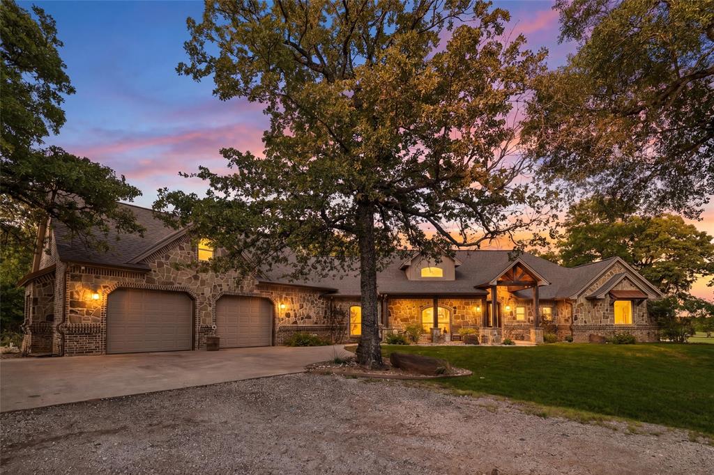 A truly rare opportunity to own one of the most unique waterfront ranch properties in the highly sought-after Grandview area. Set on 23+ ag-exempt acres with exceptional frontage along a large Soil Conservation Service reservoir, this custom estate offers a combination of water, privacy, mature oaks, usable pasture, and quality improvements that is seldom found in Johnson County. A gated entrance with cattle guard welcomes you down a picturesque tree-lined drive to the custom stone and brick residence, thoughtfully positioned to capture breathtaking water views. The property’s defining feature is its extensive shoreline, private dock, and winding stone pathway to the water’s edge, creating a setting that feels more like a private retreat than a traditional ranch property. Whether fishing from the dock, watching wildlife along the shoreline, or enjoying spectacular Texas sunsets across the water, the setting is truly exceptional. Designed for both entertaining and everyday ranch living, the outdoor amenities include a resort-style gunite pool with diving board and sun shelf, natural landscaping, and a cathedral-ceiling screened porch overlooking the water. Inside, the home features vaulted ceilings with decorative wood beams, a private office with built-ins, an oversized utility room with dog wash, and a highly desirable floor plan that includes both the primary suite and a secondary bedroom with private ensuite bath. A private upstairs guest suite with separate access, living area, full bath, and kitchenette provides ideal accommodations for guests, extended family, or multigenerational living. The ranch is fully fenced and livestock-ready with quality pasture, a loafing shed, and an agricultural exemption already in place. Combining exceptional water frontage, recreational appeal, privacy, and a premier location, this is more than a home—it’s a legacy ranch property offering a lifestyle and setting that rarely becomes available in Grandview.