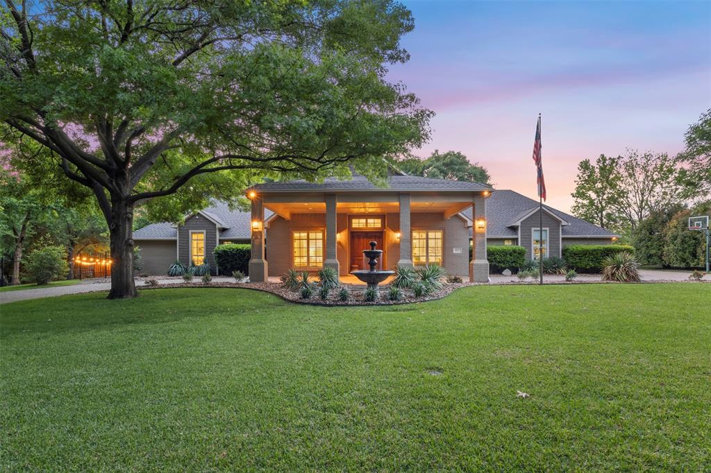 Fully reimagined sprawling single-story estate on a rare 1-acre creek lot with no HOA, tucked at the end of a private cul-de-sac in the heart of Frisco. Opportunities of this scale and setting are exceptionally limited, offering a rare blend of privacy, space, and proximity. A circular drive and porte cochère create a refined arrival, framed by mature trees and expansive grounds that feel worlds away. Taken to the studs and thoughtfully redesigned, the 4,492 SF residence is filled with natural light and defined by European white oak flooring and elevated, timeless finishes throughout. The single-story layout offers both openness and intentional separation, with four bedrooms—each with its own en suite—alongside a dedicated office, multiple living areas, and a private gym. A guest suite is further distinguished by hand-beveled wood flooring. The kitchen serves as the heart of the home, anchored by a statement island and appointed with a SubZero refrigerator, gas range, abundant custom cabinetry, and striking quartzite countertops with a full-height quartzite backsplash—equally suited for intimate daily living or elevated entertaining.
The primary suite is a true retreat, featuring generous scale and dramatic wall-to-wall windows overlooking the manicured grounds and pool, while a rare secondary primary suite offers its own private patio with direct backyard access—ideal for guests or multigenerational living.
Outdoors, the experience is resort-caliber, with manicured mature trees, turf, and layered landscaping surrounding a saltwater pool finished in PebbleTec. A 540 SF covered patio with wood-burning fireplace and motorized shades creates seamless indoor-outdoor living designed for year-round enjoyment. Modern convenience is seamlessly integrated with Lutron lighting, extensive system updates, a 3-car garage, tornado shelter, and multiple storage rooms—delivering a rare combination of luxury, comfort, and livability in one of Frisco’s most desirable locations.