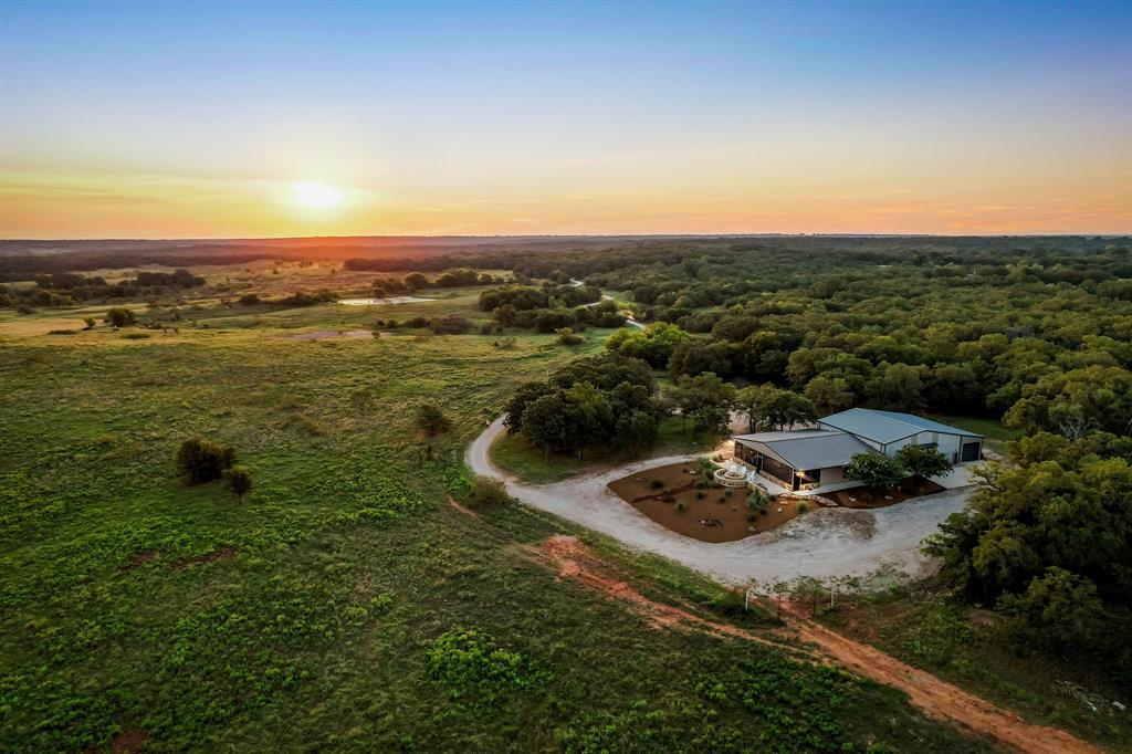 JUST IN TIME FOR HUNTING SEASON! Experience the best of Montague County with this 138± AC turn-key ranch retreat complete with a beautiful, high-end barndominium. Foxhole Ranch is located less than 1.5 hours from DFW and just minutes from the charming, historic town of Saint Jo. This property offers the ideal blend of hunting, recreation, and comfort, anchored by Turkey Creek with 5 additional ponds that provide reliable surface water for wildlife and livestock. The land features a mix of hardwood timber, open pasture, rolling terrain, and an extensive trail system. Whitetail deer, turkey, and other native game thrive in the mix of oaks, pecans & elms. The property includes several blinds and feeders already in position, giving sportsmen a true ready-to-hunt setup. At the center of the ranch is a custom 2-bedroom, 3-bathroom barndominium that comfortably sleeps 11+ guests. Designed for functionality and entertaining, it features an expansive game room with vaulted, wood ceiling and bar, a dedicated ammunition room, and a full laundry room. The living spaces extend to the outdoors including a screened-in porch with built-in propane grill and granite bar and a built-in firepit with panoramic sunrise and sunset views. The drive-through garage for vehicles and equipment is conveniently attached to the barndominium for easy access. The residence was fully designed and furnished by a professional designer can be sold fully furnished, allowing for immediate use as a weekend retreat, hunting lodge, or family getaway. The ranch is accessed through a gated entry, offering both security and privacy. Nearby Saint Jo provides charm and convenience with its historic square, wineries, and live music venues. Even better? The ranch is surrounded by several large acreage neighbors providing privacy. Currently ag exempt. NO PIPELINES. NO MAJOR TRANSMISSION LINES. NO WIND FARM VISIBLE FROM PROPERTY!