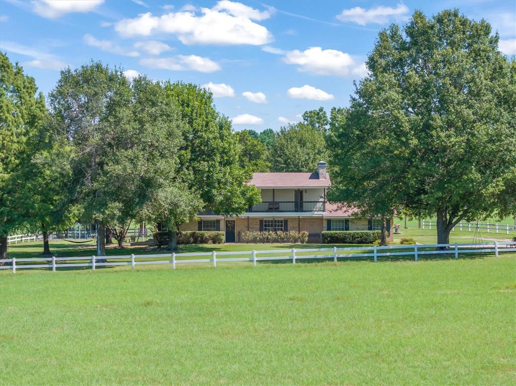 Welcome to this well-maintained 3-bedroom, 2-bath farmhouse nestled on approximately 21 pristine acres featuring an exquisite pond and mature hardwood trees. A tree-lined driveway leads you to the home, perfectly framed by its natural setting. Step inside the spacious living room, highlighted by a beautiful brick wood-burning fireplace. The primary suite offers its own brick fireplace, along with a bathroom featuring dual vanity entrances, a tub, and a separate shower. The kitchen provides generous counter space, a cozy breakfast nook, and easy access to a laundry room and craft room tucked just around the corner. Upstairs, you will find two bedrooms connected by a Jack-and-Jill bath, plus a versatile room with balcony views of the landscaped yard that is ideal as a bonus room, game room, or even a fourth bedroom. Additional features include a 10x24 enclosed storage building with a 20x24 overhang, and ample outdoor space for recreation or expansion. The well for the property was drilled in 2021. With its peaceful setting, functional layout, and thoughtful details, this property offers both comfort and country living at its finest.