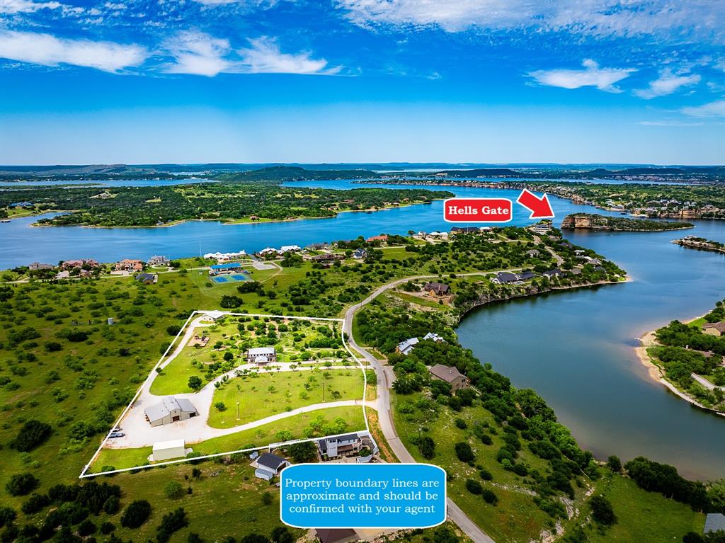 Perched on nearly 6 acres of fenced, landscaped-yet-natural terrain overlooking Possum Kingdom Lake’s iconic Hell’s Gate Cove, this extraordinary estate offers the perfect blend of privacy, adventure, & luxury living. Tucked away in a secluded setting that feels miles from anywhere, the property features rolling hills, scenic ATV trails, breathtaking lake views, & endless room to roam—all without ever leaving home. The beautifully maintained main residence greets you with a covered drive framed by a charming rose garden & opens into a warm, inviting interior with a cozy fireplace, & open-concept living-kitchen area designed to capture stunning views. The home offers 3 bedrooms, 2 bathrooms, & a spacious primary suite complete with wrap-around deck overlooking the surrounding landscape & lake. Recent updates include new HVAC systems & Trex decking (2023), water heater (2021), & new carpet (2025). A separate bonus home, built in 2024, adds exceptional space for guests, extended family, or rental use, features 1,200 sq ft on the main level plus a 500sqft loft. Designed for comfort & efficiency, the structure is fully spray-foamed for enhanced energy performance & superior insulation. For hobbyists or outdoor enthusiasts, the impressive 5,000sqft shop & garage is truly one of a kind. Complete with multiple overhead doors, expansive storage, an auto lift, & ample room for boats, ATVs, vehicles, tools, & toys, the space also includes a private 700sqft loft gym with incredible views. Kids will love the custom playground-essentially your own private park-featuring a merry-go-round, geodome climber, & 3 oversized playhouses with slides & swings. Platted as a residential estate lot, the property also allows horses, adding even more possibilities for recreation. This rare Possum Kingdom Lake retreat combines natural beauty & limitless opportunity in one unforgettable property. Come experience the breathtaking views, peaceful surroundings, & unique lifestyle this estate offers.