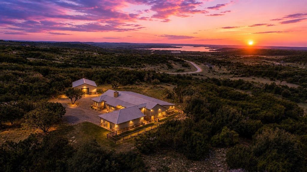 Perched high above Possum Kingdom Lake, this extraordinary 3,400 sq ft estate sits on 5.74 private, treed acres at the end of a quiet cul-de-sac in the beautiful Hills Above Possum Kingdom. The quaint town of Graham is a quick 20 minute drive away for shopping and services. The Hills Above Possum Kingdom has many amenities to enjoy, including a spectacular Pool overlooking the lake, meeting & party space, boat launch & boat storage to name a few. 
This custom home is designed to flow seamlessly with the natural terrain. This stunning 3 bedroom, 3 bath residence offers refined comfort and thoughtful functionality throughout. A 572 sq ft mother-in-law suite with kitchen, closets and walk-in shower provides ideal guest accommodations, while the primary suite features an oversized roll-in shower, heater, and a 118 sq ft closet with direct laundry access. The 3rd bedroom is designed as 2 bedrooms without a wall with murphy bed, two closets. Owner uses this space for a workout room.
The heart of the home showcases 1,255 sq ft of open living, dining, and kitchen space complete with surround sound, stained concrete floors, rock fireplace, and a stunning 16-foot double sliding door opening to a 600 sq ft covered patio. Outdoor living shines with in-ceiling speakers, electric screens, heaters, TVs, a 17-foot bar with sink and high-end grill.
The professional kitchen is equipped with Thermador Range with double ovens, Sub-Zero fridge freezer, pot filler, dual sinks, granite countertops, 13x4 butcher block island, expansive pantry, and a 59 sq ft wine room with refrigeration & room for 120+ bottles.
Additional highlights include 440 power, 2-220 pool & spa stub-outs, whole-home water filtration, metal roof, oversized 3-car garage, dog bath, electric dog door that leads to private courtyard and large fenced backyard, multiple outdoor plugs, soffit lighting, and a 1,200 sq ft insulated shop with full bath.
 It's time to enjoy the view - and the life that comes with it.