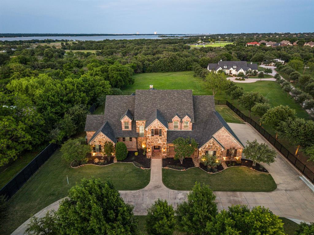 Set on nearly 2 private acres, this Maykus gated custom home offers privacy and tranquility, backing to Corps of Engineers land and just minutes from Lake Grapevine. The inviting dining room features wood beam ceilings and comfortably seats up to fourteen, ideal for both intimate dinners and large gatherings. The heart of the home is the gourmet kitchen, anchored by an expansive island and equipped with new Dacor refrigerator, dual dishwashers and a new Thermador range. It opens seamlessly to the family room, where a warm fireplace and scenic backyard views create a welcoming space for everyday living. Each bedroom includes its own ensuite bath, providing comfort and privacy for family and guests. Additional living spaces include a spacious game room and media room, perfect for entertaining. The primary suite is generously sized, featuring a well appointed bath and custom closet. Step outside to a true backyard retreat, complete with a sparkling pool and spa. The backyard is nothing short of a private resort. A sparkling pool and spa anchor the space, while a beautifully designed cabana with ample seating, a fireplace, and a pizza oven invites long, unforgettable evenings. Whether it’s a lively gathering or a quiet night under the stars, every detail has been designed to elevate the experience. This home doesn’t just live beautifully. it feels effortless, timeless and deeply connected to its surroundings.