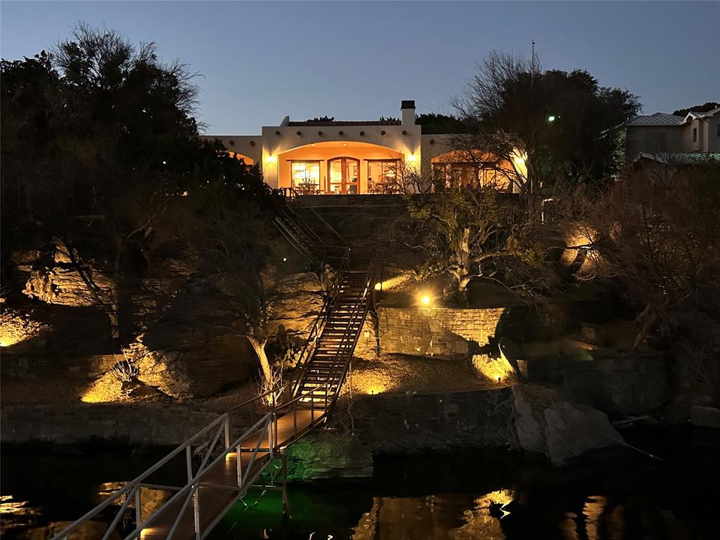 In 2020 & 2021, the home was taken down to the studs, stuccoed, rebuilt & added on to. Magnificent, upscale, single story Santa Fe style lakefront home located on the South side of the peninsula. Gated estate with paved drive, inviting covered front patios and attached carport. Instantly fall in love with the warm, inviting feel of this home. Enter through the arched front door to the welcoming foyer. It looks out to the expansive patio that extends across the lakefront side of the home, offering breathtaking views from inside and out. The spacious and luxurious great room has a vaulted beamed ceiling, fireplace, and is open to the granite kitchen with amazing pantry space. The primary suite has a shower, tub, large walk in closet & patio access. Two large spare bedrooms, (one with patio access) share a joined bath with double sinks. The huge bunk room has a full bath & split vanities.  The newer custom built two tier lighted dock includes space for two personal watercraft, boat lift, a swing that extends over the 75 foot deep channel, and plenty of room to sit and watch the sunset.