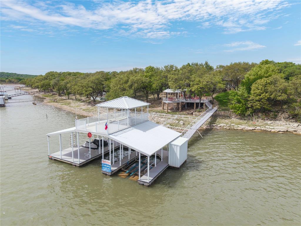 Deep-watered, fully-furnished lakefront home - including boat and jet skis - on beautiful Lake Brownwood! Bring all the family and friends! Located in Dominion Point on a heavily-treed lot - this lakefront beauty offers plenty of room with five bedrooms, three baths and lots of outdoor entertaining areas including a spacious composite-board deck cantilevered over the water. The fully-landscaped yard - completely shaded by mature live oaks - includes a sprinkler system, built-in gas grill and 12' x 12' storage building. And the gently-sloping flagstone walk provides easy access to the 30' x 48' two-slip aluminum dock with Hydro-Hoist lift, two floating jet ski ports, roomy storage closet and 17' x 30' covered sun deck. The dock floats in an estimated 18 to 20 feet of water when the lake is full. The two-story rock home includes three bedrooms (including the primary), two baths, living-dining, wood-burning fireplace, kitchen and utility room downstairs complimented by two bedrooms and a jack-n-jill full bath upstairs. All three downstair bedrooms open through French doors to a covered flagstone porch and scenic easterly views of the lake. The primary and guest baths downstairs include granite counter tops with tiled counter tops in the kitchen. The living area, kitchen, bathrooms and utility are floored in ceramic tile and all five bedrooms are fully carpeted. Park your car and golf cart securely in the two-car attached garage with electric door opener. Come home to this inviting lake-front property and stay awhile. Slow down, take your shoes off and enjoy the quiet serenity of lake living. 2008 21' Regal Boat, 2017 VC1800SA and 2007 FX Cruiser Yamaha Jet Skis convey with acceptable offer.