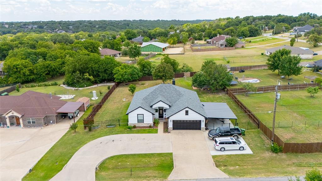 Welcome home to this recently updated home on just over a half acre in the sought after community of Indian Harbor! This home has been extensively updated in the past 3 years. New carpet in bedrooms, new paint inside and outside, 2 car attached metal carport in addition to the 2 car attached garage and with a circle driveway and concrete driveway extension added, new roof 2023, powder coated chain link fence added to the front of the property, and an enormous and aesthetically pleasing covered metal back patio on slab has been added! The basics: 3 bedroom, 2 bath, 1876 square feet, built in 2009. Located on a beautifully landscaped and treed .52 acre lot! The finer details: Oversize bedrooms throughout the home. Primary bedroom is 22X15 with secondary bedrooms measuring 15X11. Walk in closets, and ceiling fans in all bedrooms. Super size living room comes with a very pleasing stone wood burning fireplace that can heat the entire home on those cold winter days and nights. Beautiful large windows in the living room overlook the covered back patio and large back yard. Updated kitchen features granite countertops, large kitchen island, ample cabinets, and newer stainless electric appliances. Roomy breakfast area located just off the kitchen with excellent views out to the backyard. Primary bathroom features a wonderful soaking garden tub, oversized walk in shower, and walk in closet. Guest bathroom also features a separate oversized walk in shower. Exterior of home is amazing! Beautiful landscaping, large mature trees in the back yard, 30X12 workshop with electric, gutters, circle driveway, driveway extension, 2 car garage with opener and an attached 2 car carport on concrete! This home is located centrally in Indian Harbor within a short walk to the community pool, Lake Granbury, and all the amenities the community has to offer. Home is spotless clean and shows pride of ownership throughout. This home is priced to sell. Come tour and then make this home your own today.