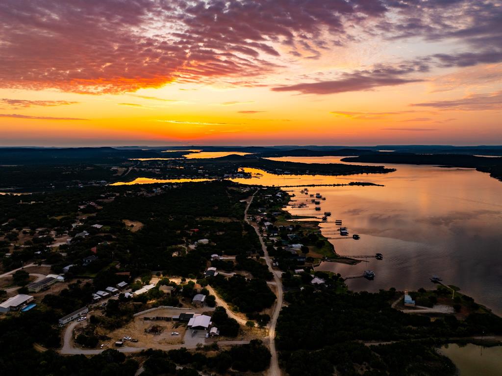 If your heart yearns for a cozy place to enjoy the amazing views of Possum Kingdom Lake and the pure peaceful bliss of life surrounded by nature, you don't want to miss this fully furnished rustic cabin located in The Retreat at Chapel Hill! Situated at the top of the drive overlooking the lake and the State Park, you will be greeted by an exquisite garden area abuzz with pollinators that will welcome you to sit and soak in the relaxation. When you're ready to head inside, the efficiency style cabin offers entry through an enclosed sunroom and extra bunk room (so you'll have room for guests) before opening up to a spacious abode.  The living area is roomy enough for settling in for your favorite movie or gather round with friends for sharing lake stories after a day on the water.  The kitchen area is separated by a convenient high-top bar that provides dining space, storage, and a great place for happy hour.  One side of the kitchen is ideal for food prep and countertop space, the other has a nice desk spot for tending to work if you must. On the opposite side of the room, there is space for a queen-sized bedroom set and a walk-in closet provides storage space.  The full-size bathroom features a shower, newer water heater, and plenty of space for changing.  This place is ideal for a weekend getaway or summer vacation home, or it could be used as a vacation rental investment property. Most furnishings, home supplies, and decor will come with the property ~ just bring your necessities and prepare to be in love with the PK Lake Life!  Short-term rental use currently prohibited; investors seeking income production would be allowed to offer a minimum six-month lease term.