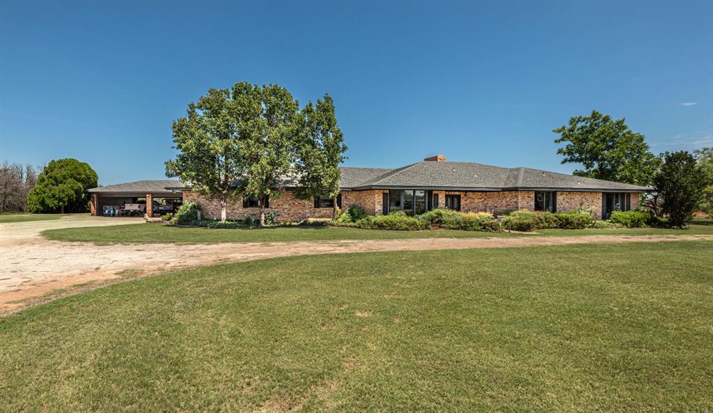A rare find, this extra-special custom-built home offers a Texas-sized 4,956 sq. ft. on 14.3 acres with space, character, and history. This expansive 4 bedroom, 3 full bath, 2 half bath home features 10ft & 12ft ceilings throughout, all primary-sized bedrooms, walk-in closets, and abundant storage. The massive living room is a true centerpiece with 12ft ceilings and a full brick wall and hearth stretching across room, a wood-burning fireplace with gas starter, and picture windows overlooking the outdoor recreation area and tennis court. The huge kitchen features a wonderful island-breakfast bar and opens directly to a comfortable den, creating an inviting everyday living space separate from the formal living & dining areas. Additional highlights include a built-in wine cooler, wet bar with sink, spacious recreation room, and large laundry room with sink. Outside, the property offers a 4-car attached brick carport, electric gate, brick entry, cattle guard, exterior security camera, and fencing with chain link and barbed wire. The back acreage extends all the way to the creek and includes the original old bunkhouse from its cowboy ranch days, adding a unique piece of history. A deer feeder in the back acreage remains. Owner would consider selling the home mostly furnished, excluding a few items. A one-of-a-kind Abilene property with Texas-sized room to roam, entertain, and make your own.