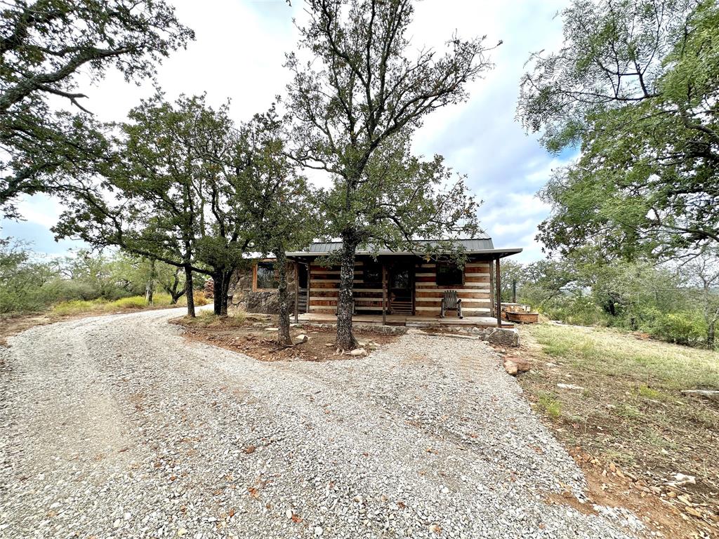 Discover the ultimate hilltop retreat in this one 0f a kind semi off grid log cabin set on 11.5 private acres in scenic Brown County. Elevated on a large hill, this 536 sq ft cabin delivers breathtaking views, total privacy, and a true unplug and unwind experience perfect for today’s high-demand short-term rental market.
The cabin offers 1 bedroom, 1 bathroom, plus a versatile loft ideal for extra guests, a remote work space, or a cozy reading nook. A standout feature is the enclosed patio style room with expansive windows, currently designed as a bold, spa-like shower space. With minimal conversion, this area could become a show stopping entertainment patio, yoga room, or sunset lounge, adding serious guest appeal.
Step onto the front porch and take in panoramic countryside view. an inviting rocking-chair space ideal for morning coffee, evening wine, and unforgettable sunsets. Infrastructure includes rural water, rain catchment system, solar power, and a 13,000 watt generator, offering reliable comfort with an eco conscious edge. An on site outbuilding provides  storage for outdoor gear and owner supplies.
Located just 10 minutes from Lake Brownwood, this property is perfectly positioned for weekend getaways, nature lovers, couples retreats, and adventure seekers. Whether you’re searching for a highly marketable Airbnb, VRBO investment, a recreational escape, or a hybrid personal use property, this elevated log cabin delivers privacy, views, and income potential in a truly unforgettable setting.