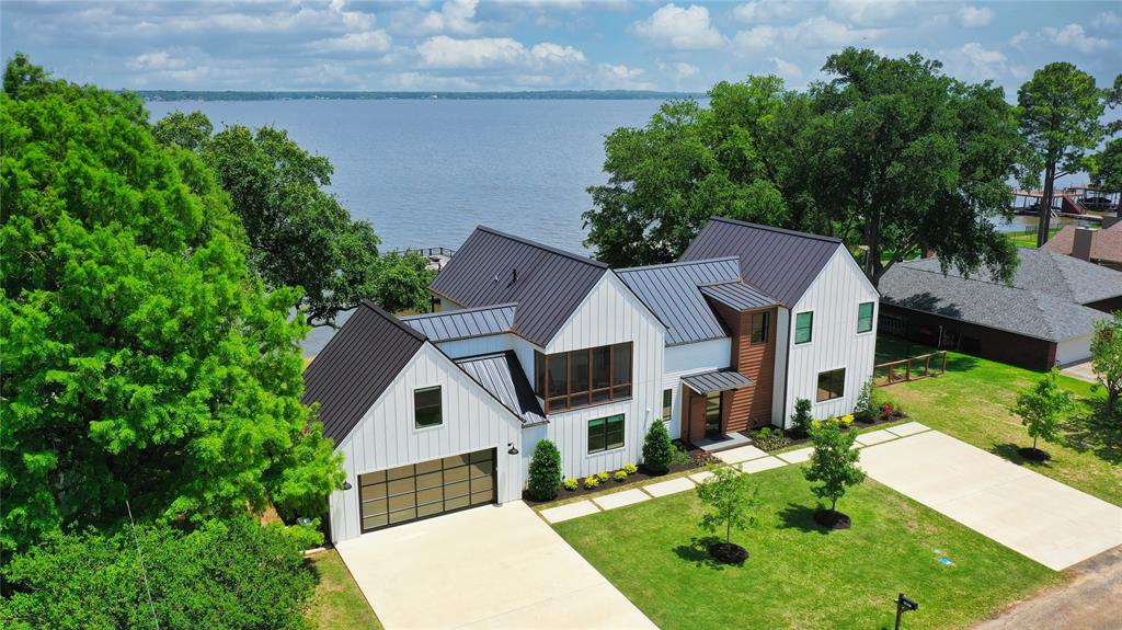 Featured in D Magazine this sprawling half acre property offers deep water and a spectacular modern style home with waterviews from almost every room. In addition to 3 ensuite bedrooms, there are 2 bunk rooms--one with 8 built in twin bunks and another with built in king bed with 2 bunk beds.  Over the garage is versatile bedroom-office-gameroom with half bath. Eat in kitchen with quartzite counter tops and cozy dining table booth. Outdoor kitchen with bar area, Green Egg, griddle, sink, ice maker and refrigerator. Watch beautiful sunrises on the expansive porch with cooling mist-bug system and motorized screens or sunsets from the screen porch on the front of the home. Relax around the firepit or take dip in the oversized Hot Springs hot tub for a perfect way to end a day at the lake. Climate controlled oversized garage plus lakeside storage for water toys. Tankless WH. Boathouse with composite decking.  Watercraft available separately.