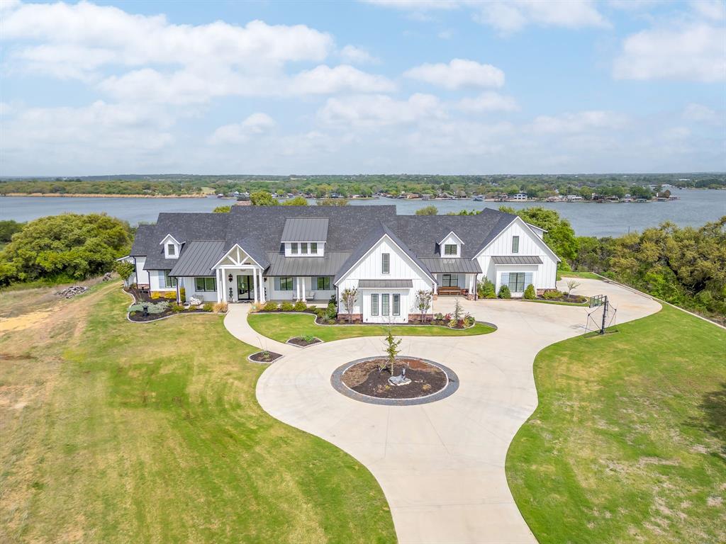 A modern farmhouse that exceeds imagination. Inviting, livable, & stunning! This exquisite custom home embodies luxury living with the most sensational views of Lake Granbury. Attention to detail was put into every aspect of this home. Step into this grand family, entertaining space with a wall of windows to capture the views. A full entertainment bar room with a sink, storage, ice machine, and refrigerators. A full prep kitchen with sink, extra dishwasher, with ample storage & counter space. The dining room captures the views at every meal. 5 en-suite bedrooms with walk-in closets. Massive laundry & craft room. Technology closet with security monitoring. 2 executive offices that are spacious & have plenty of storage. The primary suite features a cathedral ceiling, stunning views, 2 massive closets, a podcast room, and a spa-like bath with a free-standing tub & a huge walk-in shower. 4 bedrooms with baths are all on the first level. A large 5th bedroom features 8 custom-built-in bunks. A workout room and a separate workshop. There is a large upstairs storage room with a Versa Lift, so bringing your decorations up or down is super easy. 4-car oversized garages open to the side of the home. Lovely, large backyard with many amenities. A gorgeous vaulted covered porch with a fireplace, outdoor kitchen, & eating area. The pool & hot tub with views of the lake. Firepit, vegetable garden, and an adorable gardening cottage that has AC & electricity will be a favorite escape. The home was thoughtfully designed and features high-end designer fixtures throughout. Unbelievable, adequate storage throughout this home. There is even a custom doggie room under the stairs in the utility room. The circular drive with the additional parking is ideal for entertaining needs. This modern upscale farmhouse exterior is a timeless classic. So much to love about this property. Dreams can come true! Come and see this one.