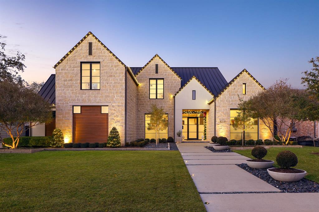 Modern Farmhouse design finds a more deliberate interpretation at 6741 Prestonshire Lane. The result is a 6,616 square foot residence that carries the ease of its vernacular roots while adding a layer of architectural discipline. Completed in 2022 by Garvey Homes, the home makes an immediate impression — limestone cladding, steeply pitched gables, and standing-seam metal roofing compose the exterior. Inside, the layout prioritizes flexibility over traditional room hierarchy. Two large-scale living areas and a media room occupy the first level in an open configuration. The kitchen centers on a Dacor Modernist suite finished in graphite: a 48-inch dual fuel steam range, combination wall ovens, and dedicated refrigerator, freezer, and wine columns that bring commercial-grade capability into domestic scale. A first-floor primary suite and adjacent guest room with ensuite bath establish the main level as entirely self-sufficient. The second floor houses three additional guest suites, a game room, and an office that allow the home to accommodate extended family or frequent guests with ease. The outdoor space blurs the conventional boundaries between interior and exterior. A substantial covered veranda incorporates an outdoor kitchen, firepit, flush-mounted radiant heaters, skylights, and motorized screens — infrastructure that reframes the veranda as primary living space rather than seasonal amenity. The heated pool, equipped with automated cleaning and cover systems, extends into a turfed backyard supported by subsurface drainage for ease & longevity. Integrated systems simplify daily life. A new security network includes AI-powered cameras and WiFi-enabled digital locks for managing entry points, while motorized window treatments and Lutron lighting interfaces serve both form and function. Electric vehicle charging stations are positioned in both garages — the three-car bay equipped with climate control for year-round functionality.