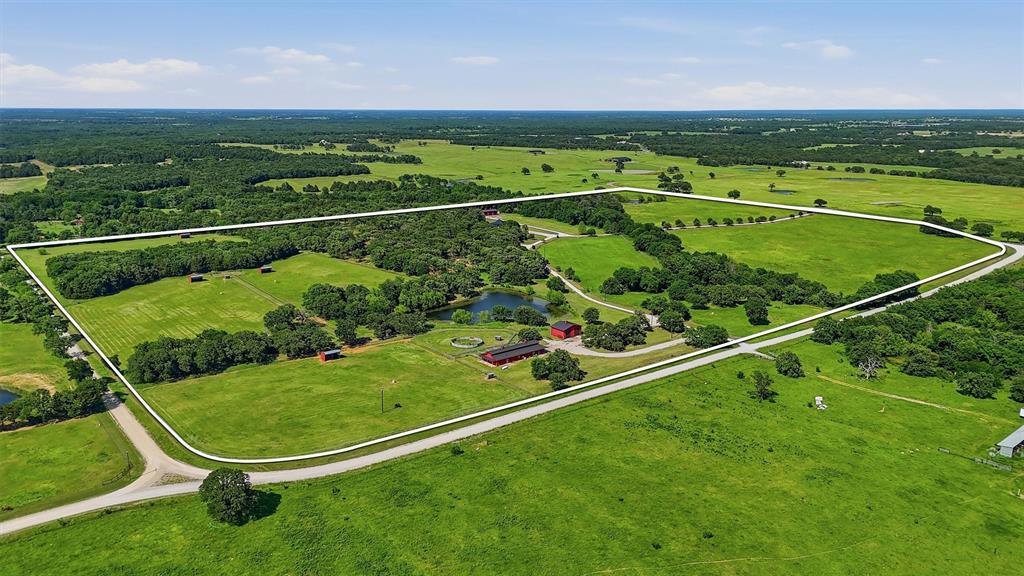 Exceptional custom ranch estate featuring a luxurious 3,118 sq ft main home, 915 sq ft guest house, equestrian facilities, and extensive upgrades throughout. The 3BR-2.5BA main residence offers vaulted ceilings with wood beams, porcelain tile floors, Lutron lighting, surround sound, and three beautifully dry-stacked gas fireplaces. Spacious living area features a dramatic stone fireplace, wood mantle, and custom French doors opening to the covered outdoor entertainment patio. Elegant dining area includes a custom crystal chandelier. Private primary suite offers surround sound, fireplace, patio access, and a spa-inspired bath with Kohler jetted soaking tub, oversized walk-in shower, dual copper sinks, granite countertops, makeup vanity, and large custom walk-in closet. Guest bedrooms share a Jack-and-Jill bath with heated floors and steam shower. Chef’s kitchen features granite countertops, custom cabinetry with cut glass inserts, copper fixtures, large island with 5-burner gas cooktop, Jenn-Air appliances, double ovens with warming drawer, walk-in pantry, and breakfast nook with tray ceiling. Dedicated wine room stores approximately 500 bottles and doubles as a reinforced safe room-tornado shelter with steel doors. Covered patio with dry-stacked fireplace, outdoor kitchen, granite counters, and multiple seating areas. Additional amenities include mahogany doors, irrigation system, Kohler generator, aerobic septic system, 3 HVAC units, mature landscaping, and attached 2-car garage. Guest house includes 2 bedrooms, Jack-and-Jill bath, full kitchen, limestone fireplace, washer-dryer and a covered porch. Equestrian improvements include a fully insulated 84x38 show barn with 7 Noble stalls, turnouts, tack room, wash rack, studio apartment, automatic waters, round pen, fenced traps, stock ponds, and feed barn. Detached 32x61 insulated shop offers 3 bays plus drive-through access. With over 5100 ft of road frontage and 2 entrances, this is country living at its finest!