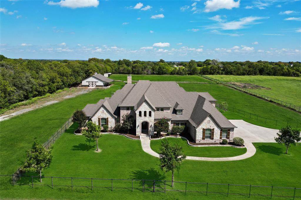 Offered on nearly eight acres with an ag exemption (for bees) in place, this custom estate combines refined living with acreage versatility and was designed with both comfort and longevity in mind, built in 2015 on 80+ piers and freshly updated with interior paint. A stone-and-brick façade with arched entry sets the tone, leading into expansive living space marked by vaulted ceilings with exposed beams, a stone fireplace, walls of windows framing serene views, and an open layout that connects the family room, breakfast space, and chef’s kitchen. The kitchen impresses with a counter-height granite island, extensive cabinetry, double ovens, pot filler, stainless appliances, and effortless flow to a breakfast nook with panoramic windows. Secondary bedrooms feature hardwood floors and bathrooms, granite counters and tiled showers, while the private primary suite offers wood floors, a tray ceiling, wall of windows to the acreage, and a spa-like bath with dual granite vanities, walk-in shower, soaking tub, and custom closet built-ins. Additional highlights include a handsome study with full-height cabinetry and French doors, walk-in pantry, abundant storage, an oversized laundry with granite surfaces, and an extra-deep four-car garage for oversized vehicles. Outdoor living rivals the interior with a covered patio, stone fireplace, pool, spa, and fenced pasture, all bordered by mature trees for privacy. For horses or livestock, the property includes fenced pastures, a 2019 Morton barn with stalls and wash bay, plus a long metal barn for storage, and holds future potential to subdivide into two additional 2-acre lots (buyer to verify with city). Blending luxury finishes with functional acreage, this estate offers an exceptional combination of elegant interiors, full equestrian amenities, and a private, versatile setting.