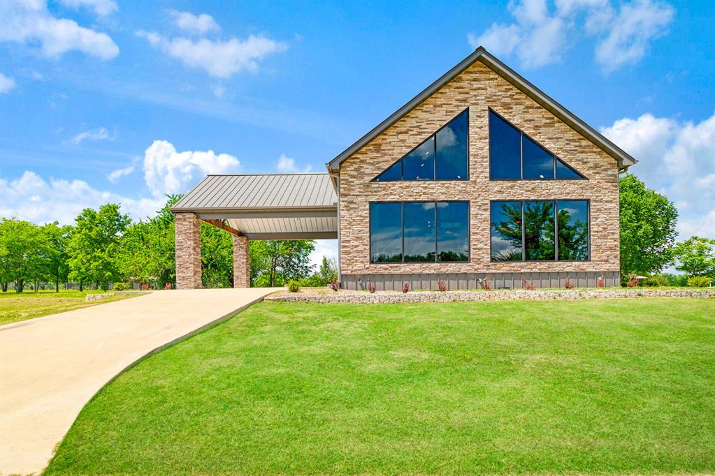Welcome home that perfectly blends modern design, rustic elegance, and spacious living. From the moment you arrive, the striking metal exterior, stone accents, and oversized covered entry create unforgettable curb appeal. Step inside to a breathtaking open-concept living space highlighted by soaring vaulted wood ceilings, dramatic floor-to-ceiling windows, and an abundance of natural light. The showstopping wall of glass frames peaceful outdoor views while creating an airy, lodge-inspired atmosphere that is both inviting and impressive. The kitchen is designed to be the heart of the home, featuring a massive granite island, custom cabinetry, stainless steel appliances, designer lighting, and ample workspace for entertaining family and friends. The expansive living and dining areas flow together, making this home ideal for gatherings of any size. The private primary suite offers a true retreat with a spa-inspired bathroom showcasing dual vanities, an oversized walk-in tiled shower, and abundant storage. Spacious secondary bedrooms provide comfort and flexibility for family and guests. Upstairs, you'll find an additional living area that adds incredible versatility to the home. This space is perfect for a game room, media room, second family room, or private retreat. Also located upstairs is an additional bedroom that could easily serve as a home office, craft room, fitness space, playroom, guest suite, or hobby room, allowing you to customize the home to fit your lifestyle.  Enjoy a generous yard space, and a covered outdoor living area perfect for relaxing evenings, entertaining guests, or simply enjoying the peaceful surroundings. This exceptional property offers the perfect combination of modern farmhouse style, luxury amenities, and functional living spaces, creating a home that is as stunning as it is practical. Whether you're looking for a private retreat, a place to entertain, or your forever home, this remarkable property delivers on every level.