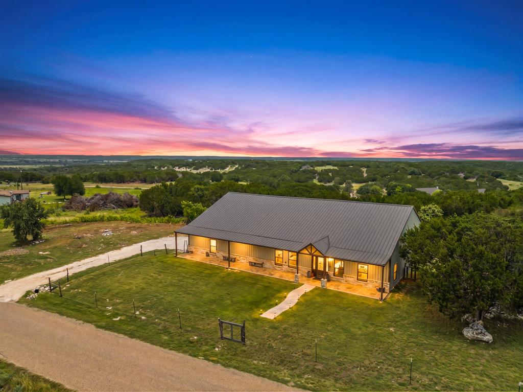 Perched atop three scenic acres with breathtaking panoramic views, this custom-designed barndominium offers the perfect blend of modern luxury, functionality, and Texas Hill Country charm. With 4 spacious bedrooms, 2.5 baths, and a versatile bonus room currently serving as a home gym, this property provides the flexibility for a 5th bedroom, game room, media room, or home office to fit your lifestyle.
Step inside to discover thoughtfully selected upgrades throughout, including a chef-inspired kitchen featuring double ovens, abundant workspace, and an open-concept design ideal for entertaining. The inviting living area is anchored by a beautiful electric fireplace, creating the perfect atmosphere for relaxing evenings at home.
Built with energy efficiency in mind, the home features foam insulation throughout, helping maintain comfort year-round while keeping utility costs in check. A spacious 3-car garage offers ample room for vehicles, equipment, and storage.
Outside, the amenities continue with an RV carport complete with full 50-amp electrical service and septic hookup, making it ideal for guests, travel enthusiasts, or additional convenience. The self-sufficient water well provides a dependable water source, enhancing the property's independence and appeal.
The true showstopper is the setting. From its elevated position, you'll enjoy sweeping Hill Country vistas that stretch for miles in every direction. Start your mornings with stunning sunrises and end each day watching spectacular Texas sunsets paint the sky with brilliant shades of gold, orange, pink, and purple. Whether you're sipping coffee on the porch, entertaining guests, or simply unwinding after a long day, the views create an unforgettable backdrop that changes with every season.
This exceptional property offers the rare opportunity to enjoy luxury living, modern efficiency, and some of the most captivating views Texas has to offer—all from the comfort of your own hilltop retreat.