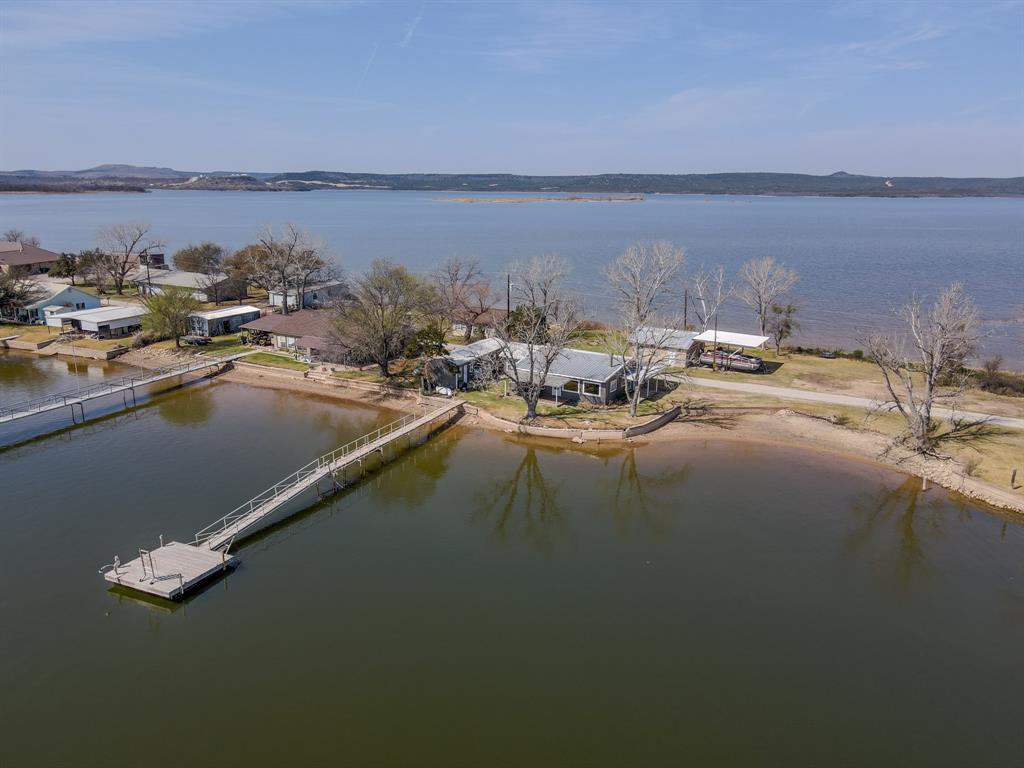 This is the kind of lakefront families talk about for years. Tucked inside a calm no-wake cove and surrounded by water on both sides, this rare double-waterfront retreat is designed for pure enjoyment. Mornings begin slowly here. Coffee in hand while the lake mirrors the sky, kids already barefoot in the sand. The private sandy beach becomes headquarters for paddleboard launches, cannonballs, sunbathing, and long, unhurried afternoons along the shoreline. The swim dock turns into evening central. Lines drop into the water for nighttime fishing, laughter carries easily across the quiet cove, and the calm water makes swimming, floating, and learning to boat feel safe and easy. This is lake life without the chaos.  Peaceful, protected, and truly usable. Inside, lake views greet you from both the primary suite and guest spaces, so the water is the first thing you see each morning. The detached guest house, with two bedrooms joined by a Jack and Jill bath, creates a private retreat for visiting family and friends, giving everyone their own space while keeping the gathering close. After long days on the water, use the outdoor showers to rinse off sunscreen and sand before dinner on the patio.