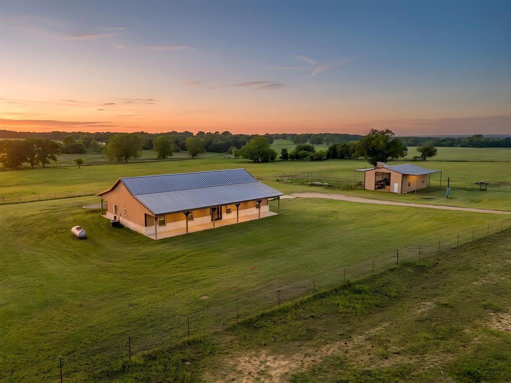 If you've been looking for space, functionality, and a property that can truly do it all-this is it. This barndominium-style, wood-framed home sits on 20 fully fenced and cross-fenced acres with two cattle pens, making it ideal for livestock, hobbies, or simply enjoying wide-open country living. Inside, the 2 bedroom 2.5 bath layout offers a smart split-bedroom designed with generous closets and room to spread out. The main living area features eye-catching tim ceilings and stained concrete floors-both stylish and built for easy maintenance. The kitchen is made for real life and entertaining, with granite countertops, a copper farmhouse sink, pot filler, abundant workspace, and beautiful decorative lighting over the island. Copper sinks in the bathrooms contniue the custom, high end feel. You'll appreciate the practical details too-a laundry and mudroom with built-ins and a sink to keep things organized, plus a half bath with direct outdoor access, perfect for working outside or future pool plans. The 30x40 shop opens the door to endless possibilities, complete with electric, water, laundry hookups, and a kitchenette-ideal for projects, a business, or guest space. RV hookups with electric and water add even more flexibility. Whether you're running animals, working from home, or just want room to breathe, this property gives you the lifestyle you're looking for.