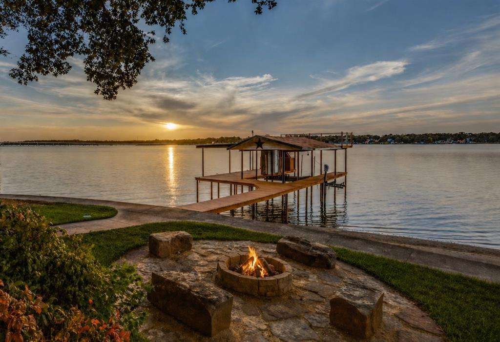 Positioned on open water, this lakefront home delivers a rare combination of usable space, flexibility, and income potential that stands out in its category. While officially a 2-bedroom, it lives like a 3-bedroom with a bright enclosed sunroom that adds meaningful flexible square footage—ideal as a guest room, bunk space, second living area, or office (not reflected in tax records). Combined with two pull-out queen sleepers, the home comfortably accommodates up to 8 adults, making it highly functional for both personal use and hosting.
Currently operating as a successful Airbnb, the property offers built-in income potential and can be sold fully furnished for a seamless turnkey transition. There is also a clear path to additional value, with the detached two-car garage already plumbed for a bath, offering the opportunity to convert it into a true third bedroom and additional bathroom, creating a separate bunkhouse or guest suite that would further enhance both livability and rental performance.

Outdoor living is equally impressive, with a fully fenced yard and gated entry, expansive driveway with plenty of guest parking, and a two-car carport currently functioning as a covered sitting area ideal for grilling and gathering. A waterside stone fire pit, well-maintained boathouse with party deck seating, pontoon cradle, PWC lift, lake pump sprinkler system, and two additional storage sheds for lake toys and lawn equipment complete the outdoor amenities.

Recent seller updates include approximately $50,000 in improvements, including flooring, paint, and hardware in 2022, plus a new HVAC system in 2024 with dual-zone heating and cooling and Nest thermostats. Move in, enjoy immediately, generate income, or enhance further—this is a lake property designed to deliver from day one.