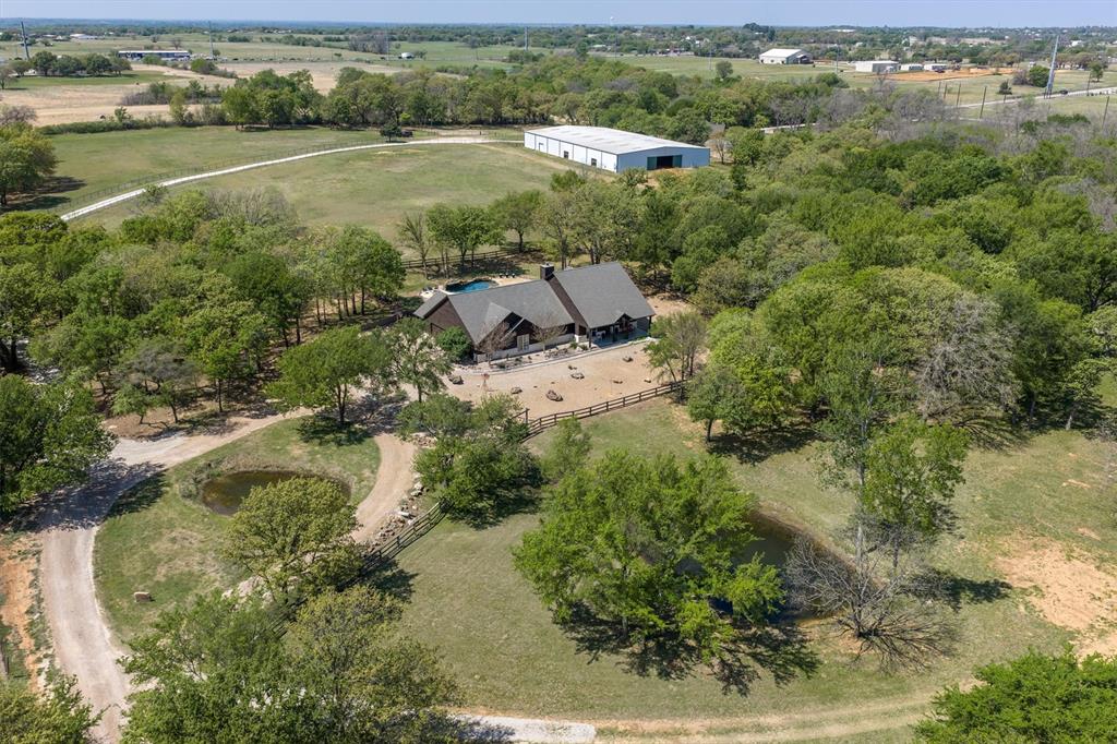 Welcome to 2431 Dr. Sanders Road in the heart of Aubrey, Texas. A perfect blend of comfort, space, and country charm. Nestled on a generous 20 acre lot, this beautiful property offers the peace and privacy of rural living while still being conveniently close to shopping and dining. Step inside to discover a thoughtfully designed layout featuring spacious living areas, abundant natural light, and stylish finishes throughout. One of the home’s most captivating features is the view. Enjoy scenic surroundings from every room, creating a bright, open feel and a constant connection to the beauty of the outdoors. The kitchen serves as the heart of the home, offering ample counter space, stainless steel appliances, and a seamless flow into the dining and living areas, ideal for both everyday living and entertaining. The primary suite provides a relaxing retreat with a well-appointed ensuite bath, plenty of closet space, and tranquil views to start and end your day. Additional bedrooms are generously sized, each offering their own inviting perspective and flexibility for family, guests, or a home office. Equestrian enthusiasts and hobbyists alike will appreciate the impressive 20,000 sq ft barn, complete with an indoor riding arena, a fully equipped shop, bonus space with a bathroom, and a dedicated tack room. The property also features an outdoor arena, providing the perfect setup for training, riding, or hosting events. Adding even more value, the property benefits from an AG exemption, offering potential property tax savings while supporting agricultural use. Outside, enjoy wide-open Texas skies from your backyard perfect for relaxing evenings, weekend gatherings, or simply soaking in the serene surroundings. With plenty of room to grow, this property offers endless possibilities. If you’re looking for a place where every window brings in a view, and where exceptional equestrian amenities meet peaceful country living, this is the one.