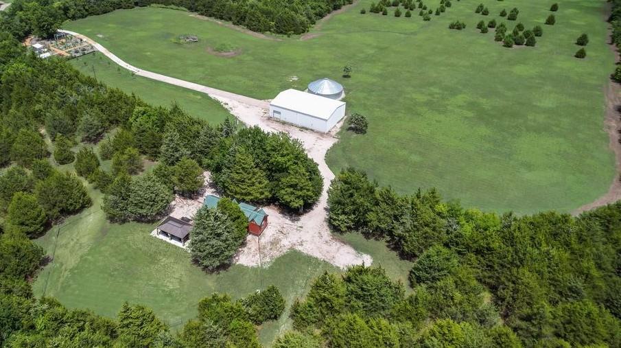 Welcome to your own slice of heaven as you enjoy your own private retreat where freedom, self-sufficiency, and outdoor adventure come together on 29.5 beautiful acres. A perfect blend of mature trees and open pasture creates a peaceful setting that feels worlds away yet offers everything you need to enjoy country living at its finest. Picturesque pastures complete with a bridge for easy access to all corners of the land with ATV trails that meander through the wooded areas, inviting endless exploration, recreation, and fun weekends with family and friends. The property features a charming completely renovated tiny home designed for comfortable living, complemented by an expanded screened-in porch that provides the perfect place to enjoy your morning coffee while taking in the sights and sounds of nature. Just outside, a welcoming entertainment pavilion area and an area for a fire pit creates the ideal gathering spot for evenings under the stars. As you drive into the property, you are greeted by the lush bee apiary full of beautiful flowers and fruit trees which not only provides a tranquil retreat but also serves as the AG exemption for the property. A custom-built Amish she-shed with custom granite counter tops, full electric and vinyl flooring for a perfect workspace. Complete RV hookup and an impressive 40’ x 60’ insulated shop offering abundant space for equipment, hobbies, storage, or business use. One of the property’s most remarkable features is its 65,000-gallon self-contained residential water system, providing independent water collection, purification, and pressure delivery without reliance on municipal services—an exceptional asset for those who value sustainability and self-reliance. Whether you’re looking for a weekend getaway, a homestead, or a private country estate, this unique property offers the rare opportunity to embrace a lifestyle of independence, recreation, and connection with the land.  Come experience the peace and privacy that await.