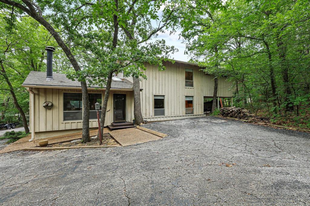 Whether you're searching for a full-time residence, weekend getaway, or the perfect place to gather family and friends near Lake Texoma, this spacious Tanglewood home offers room to spread out, relax, and make lasting memories. Situated on a large wooded lot, this 2,854-square-foot home combines comfort, functionality, and the laid-back lake lifestyle buyers love.  Designed with entertaining in mind, the open-concept main living area features a cozy wood-burning stove, abundant natural light, and seamless flow into the dining room with built-in cabinetry and the well-appointed kitchen. Complete with a large island, pantry, stainless steel appliances, and ample workspace, the kitchen serves as the heart of the home for everything from holiday gatherings to casual weekends at the lake.  One of the home's most desirable features is the rare dual primary suite layout, with a private suite on both the first and second levels, providing flexibility for guests, multi-generational living, or hosting lake weekends. In addition to the two primary suites, the home offers three additional bedrooms and multiple living spaces designed to accommodate a variety of needs.  A second large living area upstairs creates the perfect game room, media room, or gathering space, offering room for everyone to enjoy their own activities while still staying connected.  Step outside and enjoy the peaceful setting from the covered back deck or gather around the fire pit under the shade of mature trees. The large lot provides privacy and plenty of space for outdoor entertaining. A one-car garage and three covered carports offer exceptional storage for boats, golf carts, and all your Lake Texoma toys.  Located in the desirable Tanglewood area near golf, dining, and Lake Texoma recreation, this property offers the space, flexibility, and lifestyle that make lake living so special.