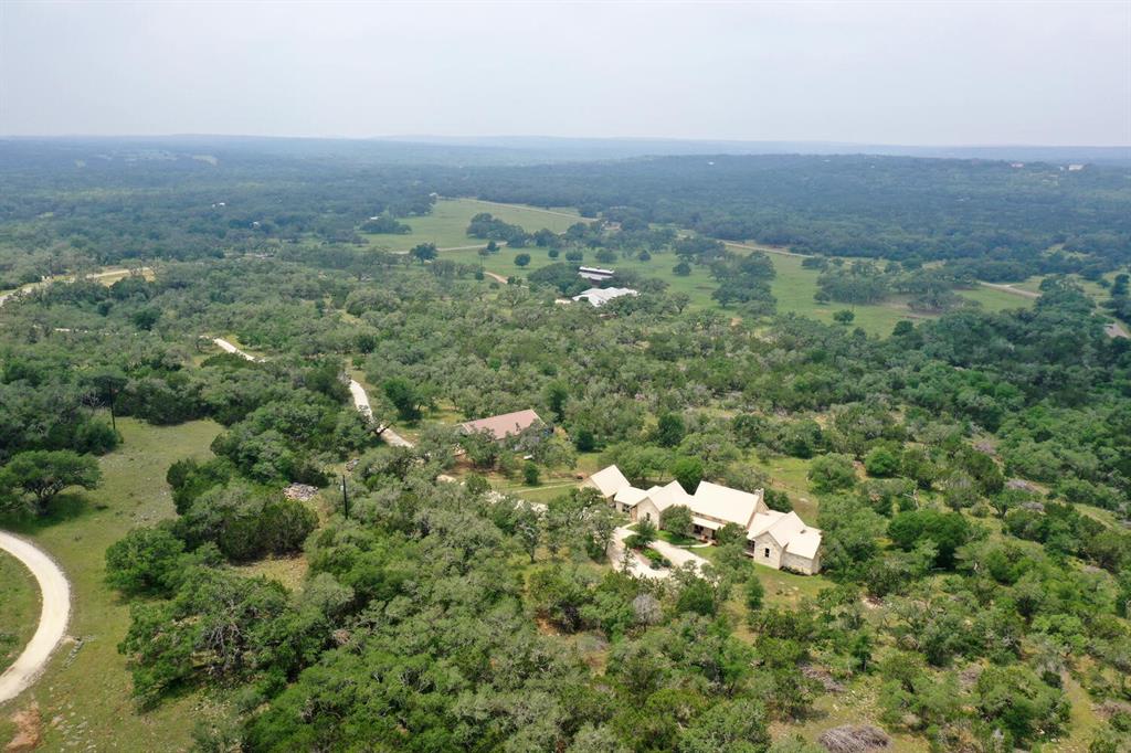 Stunning 24-acre gated estate in Bridlewood, tranquil retreat 10 mins from Wimberley Square & San Marcos-I35. Homeowners can choose between ag exemption with roaming cattle or separate fencing & switching to wildlife exemption. 3,322 sqft single-story home boasts 3 beds, 2.5 baths, office, & 2 living rooms. Designed by Charles Roccaforte, it showcases hickory floors, 18+ ft ceilings, & elegant fixtures. Master bedroom features sitting room & direct access to spacious back patio. Surrounded by woodlands, the large covered porch offers breathtaking views. Property includes a 40'x60' toy-equipment barn with 38'x12.8' air-conditioned space for storage & recreation. Conveniently located 45 mins from Austin & San Antonio, enjoy city amenities with a peaceful countryside setting. Choose between Wimberley ISD or San Marcos ISD for schooling, with San Marcos Academy nearby. Priced to sell at $1.998M, this estate offers attention to detail, high-end features, & Hill Country living at its finest.