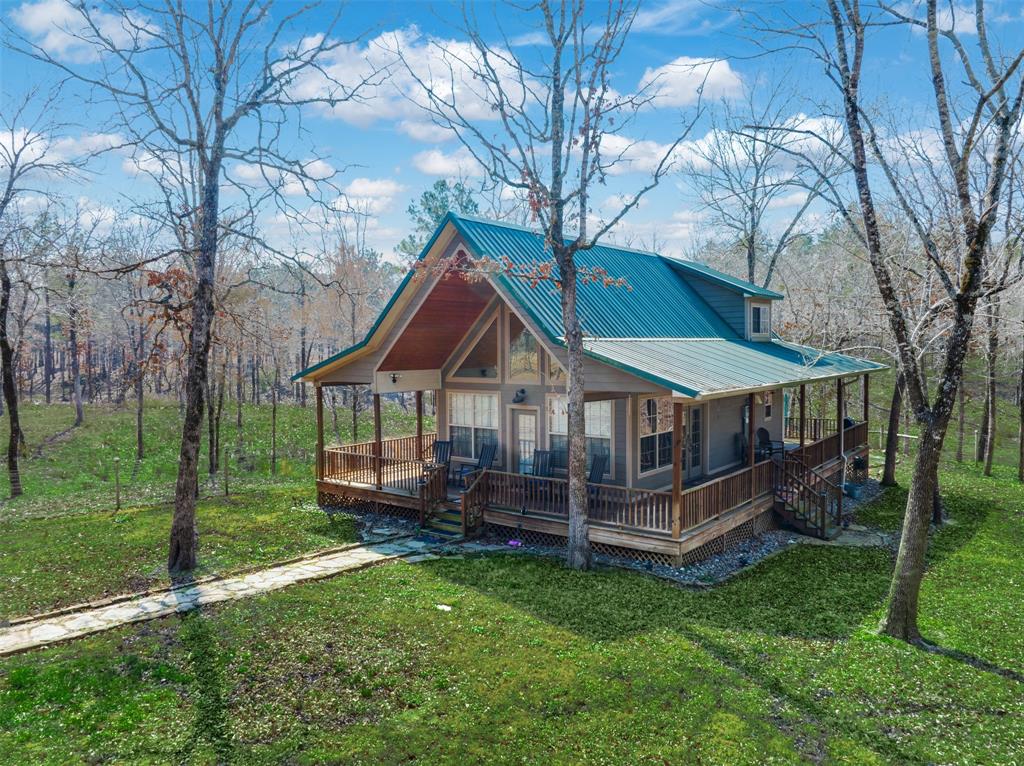 Situated on 106.030 acres, this charming rustic cabin, custom built in 2010, welcomes you via a stone sidewalk and capturespicturesque views from its complete wraparound porch. Inside, cedar walls, vaulted ceiling, & stairway plus floor-to-ceilingwindows flood the open living, dining, kitchen, pantry, loft bedroom, and bath with natural light. The flooring—reclaimed froma 100-year-old school in Dallas—adds warmth, character, and history to the thoughtfully designed interior. Smart storagesolutions maximize space, while the Hardie concrete siding exterior ensures low-maintenance durability. Within the fencedhomesite, a cozy firepit creates the perfect setting for cool evenings under the stars. Additional improvements include a 1,500± sq. ft. metal garage and storage building, plus an 864± sq. ft. open shed for equipment or recreational vehicles.Approximately 15 acres of high-fence pens (7 total) with a surrounding high-fence alley were previously used for raising deer,offering continued wildlife or livestock opportunities. The land has been enhanced with 130 loads of dirt to prepare for ahomesite or barn, providing flexibility for future expansion. Fields have been planted in drought-resistant millet sorghum tosustain wildlife, with established white clover and Bermuda grasses adding to the agricultural appeal. Peach, apple, and figtrees have also been planted for personal enjoyment. Whether you envision a private retreat, recreational ranch, wildlifeoperation, or future homestead, this remarkable property offers endless possibilities—an extraordinary sanctuary that reflectsthe restorative beauty and peaceful charm of East Texas living.