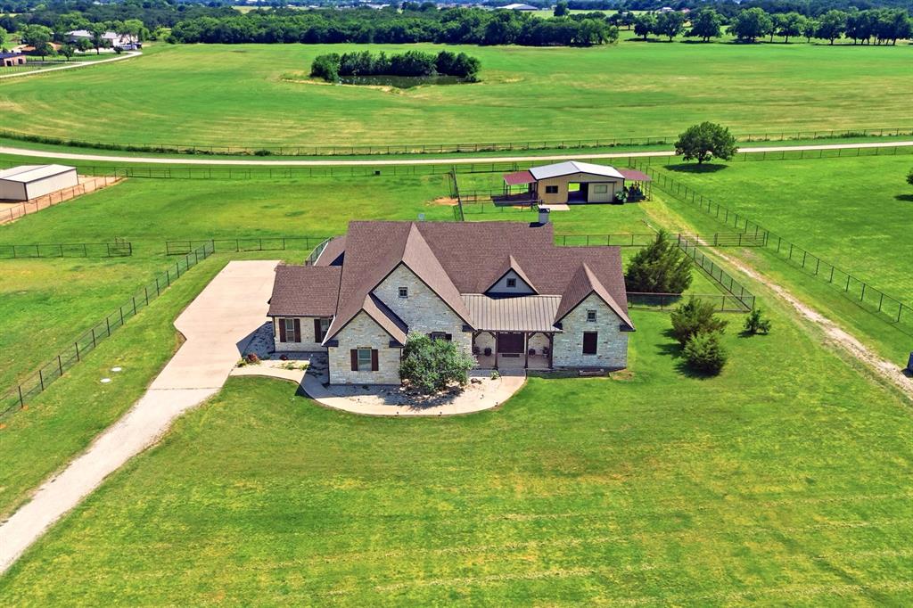 10040 Horseshoe Nail Road is a refined ranchette offering a beautifully maintained custom home and stable on 2.57 acres in a quality deed-restricted acreage neighborhood between Aubrey and Pilot Point.  Built in 2013 and recently updated, the stone custom home offers approximately 3,150 square feet of thoughtfully designed living space highlighted by abundant natural light, generous window space, 10-plus-foot ceilings, hardwood floors, and stone countertops. The single-story floorplan is centered around a welcoming living room with an 18-foot vaulted beamed ceiling and stone fireplace that opens to a spacious kitchen featuring an island, breakfast bar, gas cooktop, walk-in pantry, and adjoining dining area.  The home includes three ensuite bedrooms, two of which are primary suites, plus an oversized guest bedroom and a flex room with a closet, ideal for a home office or fourth bedroom. A powder bath serves the main living area. The oversized three-car garage features a full stairway leading to a large, floored attic, providing exceptional storage space. A roomy covered back patio extends the living space outdoors.  The property is well-suited for horses, with a 24×36 barn featuring a concrete center aisle, an insulated roof, three stalls, and a tack room. Two stalls open to partially covered lots with access to two larger pipe-fenced pastures. The sandy loam soil and separate barn driveway add to the property’s functionality.  Located in a small neighborhood of custom homes and horse properties, the setting offers convenient access to Denton, Frisco, North Dallas, the new PGA resort and golf courses, Lake Ray Roberts, riding trails, hospitals, universities, airports, and major corridors, including the Dallas North Tollway and I-35.