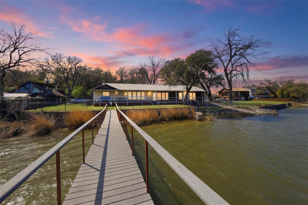 Rarely offered on the shores of Lake Worth, this private waterfront retreat offers the lake lifestyle buyers are searching for. Set on a large lot surrounded by natural beauty, the home is designed to capture stunning water views while providing comfortable living and great entertaining space.  The home features 3 bedrooms, 2.5 baths, two living areas, formal dining, and an open kitchen with island and granite countertops. The large primary suite offers dual walk-in closets and a spacious bath with a huge walk-in shower.  A wall of windows across the back fills the home with natural light and frames beautiful lake views. Step outside to the full-length composite porch that spans the back of the home—perfect for relaxing or entertaining with minimal maintenance.  For lake lovers, the property includes a personal boat ramp and a rare enclosed double boat house with lifts and a floating boarding dock. Composite decking and built-in speakers make enjoying time on the water easy and low maintenance.  The large lot extends up the hill for additional parking and includes an attached double carport plus a detached two-story two-car garage with a double steel carport.  With good water depth for boating and jet skis, and located minutes from highways, Lockheed Martin, and about 15 minutes from downtown Fort Worth, this property offers both convenience and a true lake lifestyle.  Waterfront opportunities like this on Lake Worth are rare—schedule your private showing today.