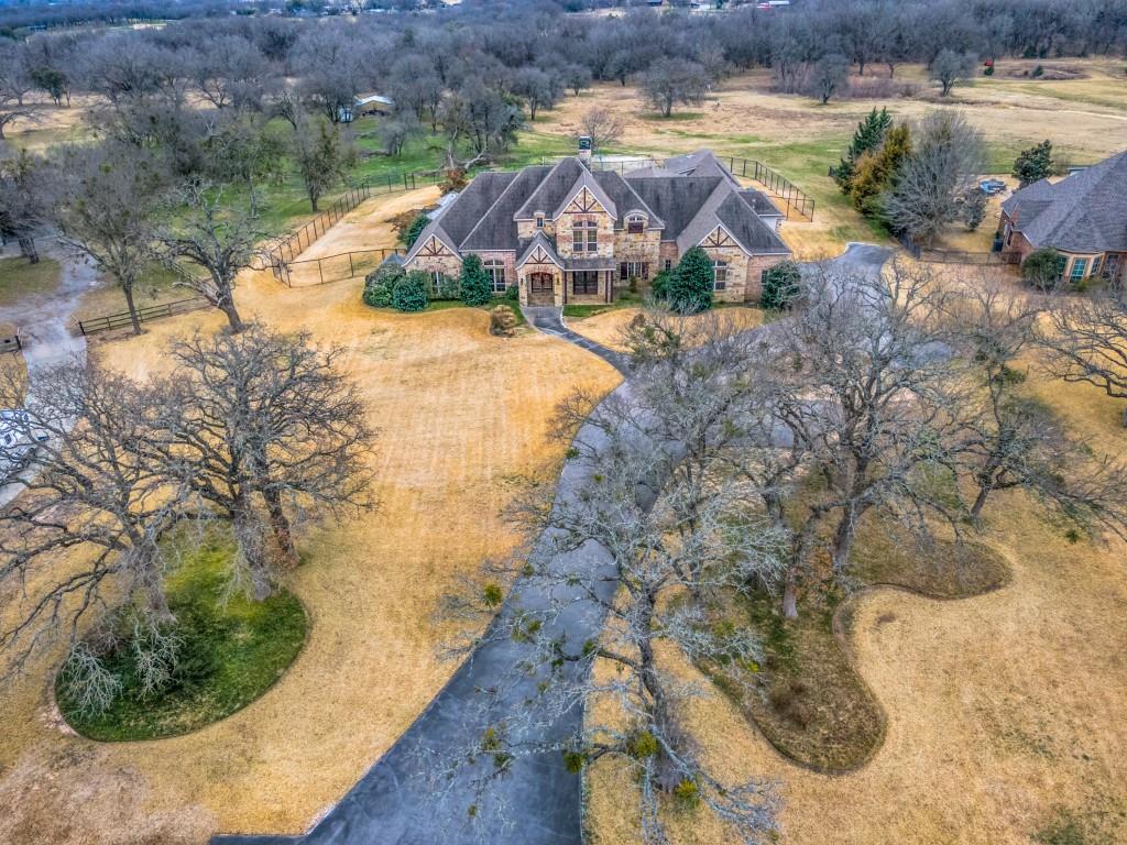 Nestled within the gated community of Ashbriar, this sprawling estate sits on almost 8 acres, offering the perfect blend of privacy, luxury, and functionality. Entering the grand two-story home you are greeted by a stunning curved staircase. The open yet defined living spaces include a front den that provide privacy for the office, a spacious dining room, and a living room featuring a see-through fireplace. The chef’s kitchen and the connected bar showcase beautiful slate floors, and is an entertainer’s paradise. The space is equipped with Wolf brand appliances, a 6-burner gas stove, an additional electric stove, 3 ovens, warming drawer and an expansive pantry. The owner’s suite offers a spacious bedroom with views to the backyard, a sprawling bathroom with a walk-in shower and separate tub.  One wing of the home includes 2 guest bedrooms with private access. There is a dedicated pet space, designed with an interior room and a pet door leading to an enclosed outdoor area. Next to the pet hotel is an additional room that is flexible living space. Upstairs, an additional living area separates three bedrooms, complemented by bonus spaces for entertainment, exercise, or added bedroom accommodations. One room opens onto a private balcony overlooking the expansive backyard and resort-style pool. An added surprise in this Texas home is the basement! Constructed with reinforced concrete it serves as both a media room and a storm shelter, offering ultimate safety and comfort. Outside in your own oasis you will find an 8-foot fenced backyard and an additional removable safety fence around the heated pool and spa. The swim-up bar and the outdoor kitchen enhance the setting for entertaining. Beyond the fenced yard, find a sand volleyball court. The property extends to the Trinity River, and offers a dug-out tank for future use. This estate is a rare opportunity to own a private retreat within a sought-after gated community in Aledo ISD.