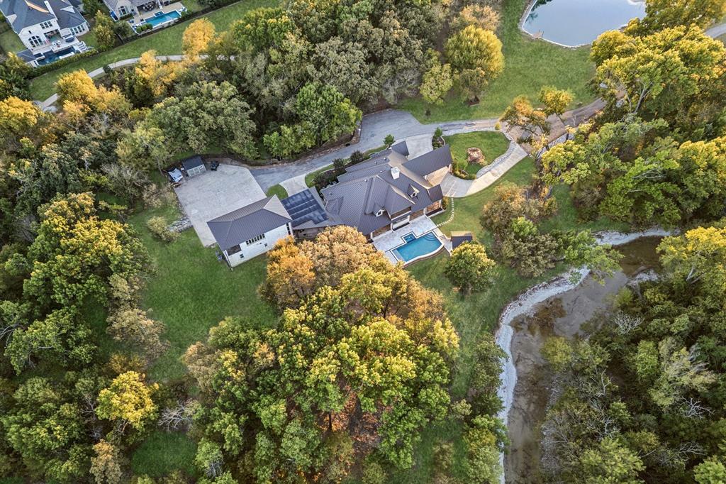 A truly rare Prosper retreat, 6604 Preston Country Lane sits on more than 6.5 extraordinary acres with waterways surrounding the property, creating a setting that feels private, peaceful, and unlike anything else. Reimagined in 2022, this estate pairs timeless architecture with modern upgrades. The main home offers 4,904sf, guest quarters 1,345sf, totaling 6,249sf. Designed to evoke the feel of a Colorado mountain retreat, the estate combines rustic elegance with refined comfort. The stucco main home is topped by a metal roof and introduced by a circle drive and dramatic porte-cochere entry. Inside, white oak flooring spans the downstairs, while knotty alder trim and cabinetry add warmth and craftsmanship. Oversized picture frame windows flood the home with natural light and capture views of the property. The kitchen is outfitted with premium appliances, large island, and elevated finishes. Two stone fireplaces anchor the living room and primary, adding warmth, texture, and a sense of timeless luxury. Outside, the estate lives like a private resort. A 1,500sf covered patio with an outdoor kitchen and fire pit creates an exceptional setting for entertaining, all overlooking the newly added Gold Medal pool finished with travertine pavers and Mexican stone. Beyond, the expanded pond and fountain enhance the beauty and usability of the grounds, while horse permission adds even more flexibility for both luxury living and lifestyle use. The detached guest quarters provides versatility with a stone wall entry, 2 bed, 2 bath, kitchen, and living area. The near complete remodel gives the next owner the opportunity to bring their own finishing selections. Matching hardwood flooring, trim, and cabinetry continue into the guest quarters for a seamless finish. An expansive carport, detached 4 car garage, RV parking, finished out playhouse, and an extra storage shed complete this offering. Solar panels atop the carport help offset energy costs. Horses welcome! No HOA.