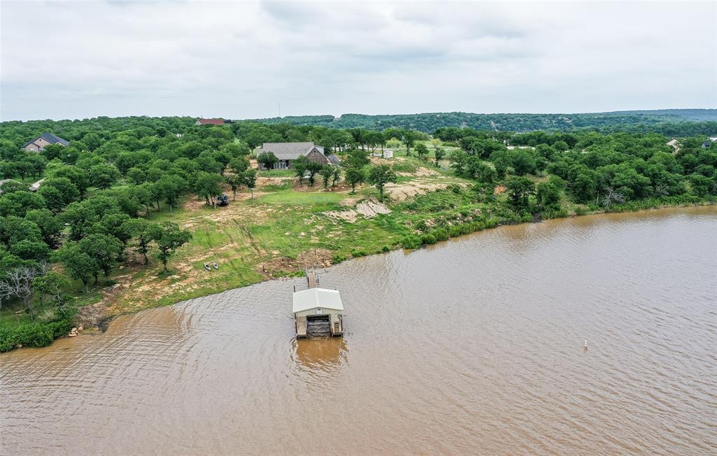 LUXURY WATERFRONT RETREAT in The Gated Community in Sunset Bay on Lake Bridgeport. Situated on 2 Private Acres with approximately 195ft of shoreline, this exceptional custom home offers panoramic water views, beach entry shoreline access, and a private boat dock with electric slip. Built in 2020, this thoughtfully designed home features 4 BedRms, 3.5 Baths, and 3,030sqft of living space. Expansive Pella Sliding Doors frame breathtaking lake views and fill the open concept living area with natural light. The spacious Family Room with stone fireplace flows seamlessly into the Chef’s Kitchen featuring an oversized island, KitchenAid Appliances, double ovens, Bosch Dishwasher, granite countertops, abundant cabinetry, and a walk-in pantry. The Private Primary Suite is designed as a true retreat, offering lake views, dual vanities, jetted soaking tub, oversized shower, large walk-in closet, and hidden storm shelter. Upstairs, the approximately 700sqftt Bonus Suite includes a Kitchenette, full bath, living area, and walk-in closet! Ideal as Guest Quarters, Bunk Room, Game Room, Second Primary Suite, or multi generational living space. Additional features include luxury Vinyl Plank Flooring, Smart Home Technology with App Controlled Lighting, Smart Thermostat, Security System, oversized 3 Car Garage with Epoxy Floors and 12ft Ceilings, 50-amp RV hookup, covered front porch, covered lake view patio, and extensive storage throughout. Enjoy boating, fishing, kayaking, swimming, and entertaining directly from your own shoreline. Sunset Bay Residents enjoy exclusive access to a Community Clubhouse, Swimming Pool, and Pickleball Courts. Conveniently located near Northside Marina with Boat Rentals, Guided Fishing, Dining, Mini Golf, and Recreation. Rare opportunity to own a premier waterfront property offering luxury, privacy, and year round lake living on one of North Texas’ most desirable lakes! Perfect as a full time residence, weekend getaway, and vacation home!