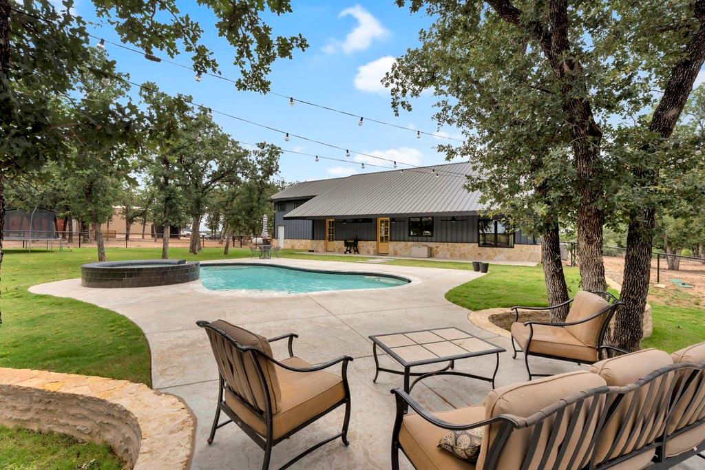 Welcome to this stunning 2024-built hybrid construction (steel structure with wood walls) masterpiece nestled on almost 10 picturesque acres, complete with a tranquil pond and mature trees. This thoughtfully designed 4-bedroom, 2.5-bath home offers 2,580 sq ft of beautifully appointed living space featuring soaring vaulted ceilings in the living room and master suite, 9-ft ceilings and 8-ft doors throughout, and polished concrete floors that add to its modern ranch aesthetic. The open-concept living area is anchored by a ventless gas fireplace and flows seamlessly into the gourmet kitchen, where you'll find an extra-large island, custom cabinetry, and a fully equipped pantry with its own power and countertop space. A custom-built media center adds the perfect finishing touch to the living room. The attached, insulated double garage (436 sq ft) features a versatile upper level with a playroom and guest bedroom — ideal for multigenerational living or a private retreat. Step outside to your resort-style backyard, complete with a brand-new pool and spa with wireless controls and a heater, a pipe-fenced yard with three walk-through gates and a drive-through gate, a sprinkler system, and an exterior entrance to the half bath — perfect for entertaining. The impressive 30x40 shop with 16-ft walls, power, and two 12x12 roll-up doors is ready for all your equipment, hobbies, or business needs. Built with spray foam insulation on all exterior walls and the roof deck, three separate AC units (including a dedicated unit for the upper level), a whole-home generator hookup, and a new well and aerobic system, this property is as energy-efficient as it is breathtaking. This is truly one-of-a-kind Texas country living at its finest — don't miss it.