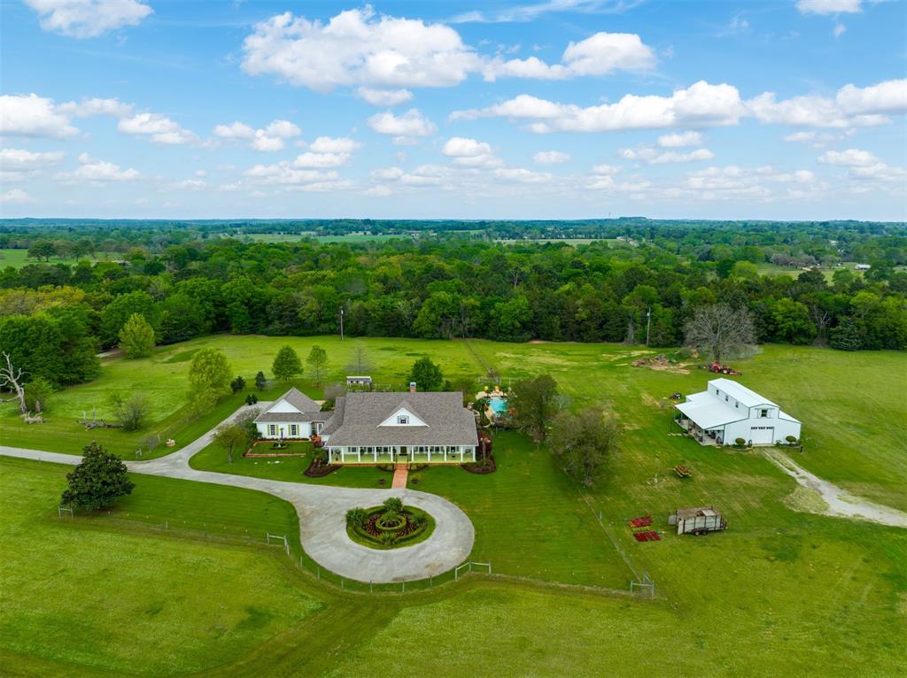 Experience timeless elegance and East Texas charm on 9.301 beautifully maintained acres just minutes from Tyler. A long,scenic drive welcomes you to this classic Southern-style estate, where a circular drive and brick walkway lead to anexpansive front porch—perfect for relaxing and enjoying the peaceful beauty that surrounds you. Step inside to a gracious,wide entry hall flanked by formal living and dining rooms, guiding you toward a beautiful staircase and inviting family roombeyond. The 3,417 sq. ft. main residence offers a thoughtfully designed layout with 3 spacious bedrooms, including two onthe main level, plus a versatile upstairs bonus room ideal as a 3rd bedroom, game room, office, or exercise space. With 3 fullbaths, multiple living areas, and two dining spaces, this home is perfectly suited for both everyday living and entertaining.Rich wood floors and abundant windows fill the home with natural light and bring the beauty of the outdoors inside. Stepoutside to discover exceptional outdoor living spaces featuring lush landscaping, flagstone accents, a sparkling pool, and acozy outdoor fireplace—creating the perfect setting for gatherings or quiet evenings under the stars. A standout feature ofthis property is the impressive 3,600 sq. ft. barndominium, complete with a welcoming 500 sq. ft. covered front porch. Inside,the 1,800 sq. ft. guest quarters showcase an open-concept living, dining, and kitchen area highlighted by a striking beamedmetal ceiling, along with two bedrooms and one bath upstairs. The additional 1,800 sq. ft. barn or garage space offers ample room for equipment, workshop, hobbies, or storage. Surrounded by exceptional landscaping, picturesque hay pastures anda variety of fruit trees, this property offers both beauty and functionality. Located in the highly sought-after and award-winningBullard ISD, this exceptional estate provides the perfect blend of luxury, comfort, and country living.
