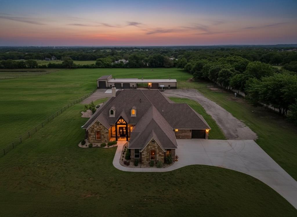 Welcome to a private estate where expansive Texas skies meet elevated country living. This custom-built residence showcases exceptional craftsmanship, upscale finishes, and a light-filled, open-concept design tailored for both everyday comfort and refined entertaining.
The gourmet kitchen is thoughtfully appointed with a propane cooktop, pot filler, wine refrigerator, beverage center, and generous counter space and storage—ideal for hosting gatherings of any size. The owner’s suite offers a peaceful retreat, featuring a spacious walk-in closet and a spa-inspired bath complete with a personal sauna and plumbing in place for a future soaking tub.
Outdoors, the resort-style pool creates a true centerpiece, featuring a tanning ledge, waterfall, and bar-top seating, all complemented by a fully equipped outdoor kitchen designed for effortless entertaining.
Set on approximately 10.25 acres of level, highly usable land with premium sandy loam soil, the property is fully fenced and cross-fenced, offering mature trees, open pasture, and well-designed turnouts suitable for horses and cattle. Equestrian and utility improvements include a 30x50 split shop with four stalls and a tack room, covered trailer parking, and a dedicated man cave with bath, providing both function and flexibility.
Ideally located in a peaceful setting just minutes from town, this exceptional property offers a rare combination of privacy, practicality, and modern luxury—capturing the very best of refined rural living.