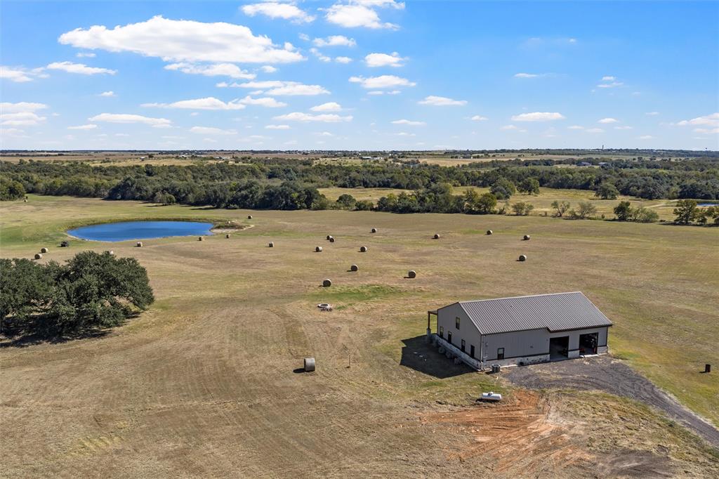 Deer Creek Ranch is one of the few true gentleman’s ranches in Central Texas that exhibits an array of natural wildlife as well as a very versatile topography to suit the outdoor enthusiast with endless opportunities. From the time you enter the main entrance you can feel the tranquility and seclusion as the outside world fades away. You are welcomed by a long winding driveway underneath the canopy of trees that opens up to the beautiful native hardwoods, established coastal pastures & lush meadows that are perfectly placed within the rolling topography of the land. Wildlife flourishes here and it is very common to see whitetail deer, duck, feral hogs & dove that frequent the area. Easily meet cattle grazing & watering needs and yield hundreds of quality hay bales per year within a fully fenced perimeter.  With multiple creek systems, 3 stock tanks, pecan & hardwood bottoms this ranch has a very natural and attractive habitat that promotes year-round hunting with ease. Easy access with two entrances from two separate county roads. Hidden within the outline of heavy woods there is an opening with a metal bridge that allows you to cross over Little Deer Creek that leads you to a secluded meadow that provides a stock tank and great chance to feel even further of the grid.  The newer built barndominium overlooks the ranch on the hilltop and offers 3 bedrooms, 2 baths, open kitchen and living area with a modern customized feel along with a large shop & garage area that can be utilized in various ways including entertaining.  The roll up doors from the shop area open to the large covered patio area that overlooks the larger stock tank with a breathtaking view. Enjoy this property as a year-round homestead, recreational retreat or investment that is sure to be the envy of anyone who visits this distinctive paradise. AG Exemption in place. No Restrictions. Centrally located between Austin & Dallas. Approximately 11 miles east of I-35 between Waco & Temple. Rosebud-Lott ISD.