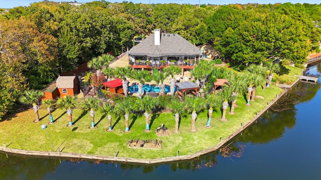 Rare, one-of-a-kind, resort-style lakefront retreat in the heart of the DFW Metroplex, tucked away on a quiet cul-de-sac and set on a beautifully landscaped .34-acre lot with direct frontage on a private lake and framed by 32 mature palm trees that create a serene, tropical atmosphere and everyday vacation vibes just minutes from town. Lush landscaping is irrigated directly from the lake, allowing you to enjoy stunning grounds without high water bills. Impressive open, light-filled living spaces designed for both everyday comfort and exceptional entertaining, including a grand living room and game room with panoramic lake views, custom wet bar, new wine fridge. The kitchen flows seamlessly into the den and formal dining area, making hosting family gatherings, dinner parties, and holidays effortless. The oversized primary suite serves as a private sanctuary with a spa-inspired bath and direct backyard access, perfect for enjoying peaceful mornings overlooking the pool, palms, and shimmering water. Step outside to your private oasis featuring a sparkling resort-style pool, flagstone decking and covered porch, expansive deck, private sauna with lighting and music, two powered gazebos, custom outdoor lighting, and breathtaking sunset views. This home offers peace of mind with a new Lennox HVAC system and condenser with 10 yr warranty, new roof, two 200-amp electrical panels, updated plumbing from meter to home, remodeled kitchen and downstairs areas, rod iron fencing, new front courtyard, 2 storage sheds including a greenhouse-style structure, 32 outdoor electrical outlets throughout yard & lakefront, custom outdoor lighting, and a 12-camera outdoor security system. An oversized three-car garage with a heated and air-conditioned half bath. More than a home, it's a lakefront lifestyle offering luxury, privacy, and comfort, where every day feels like a retreat and opportunities like this rarely come to market.