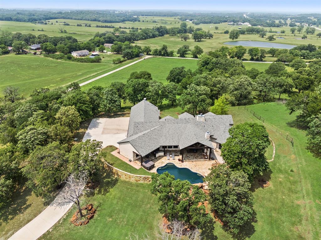 Seize this rare opportunity to own a stunning dream home nestled on a hilltop with breathtaking views of Lake Ray Roberts. Picture yourself enjoying serene evenings on the patio by the fireplace, overlooking the luxurious pool. This exceptional custom-built residence boasts a thoughtfully designed floor plan that features a gourmet kitchen, expansive entertaining areas, and a lavish master suite complete with a convenient laundry room. With three additional spacious bedrooms, a fun-filled game room, and a generously sized laundry room equipped with a dog washing station, this home truly has it all. Ideal for your livestock, the property is fully fenced and includes a barn, a shed row, pens, and ample riding space.
