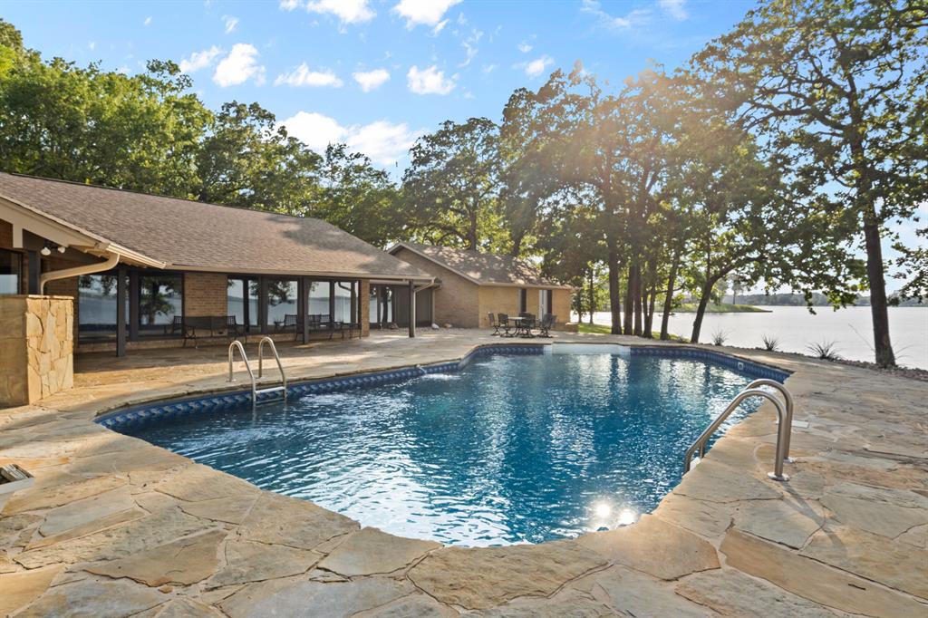 Completely reimagined inside and out, this extraordinary legacy property invites you to create generations of memories in one of Lake Bob Sandlin’s most breathtaking settings. Perched on approximately 2.5 acres at the tip of the peninsula, this rare offering boasts over 1,500 feet of shoreline, delivering unmatched panoramic water views and an unparalleled sense of privacy. With water visible from every window and multiple living and dining areas both inside and out, this nearly 4000 square foot home provides ample space for entertaining the masses. Outside, your private oasis awaits. Lounge in the shade or soak up the sun all on the expansive flagstone patio that draws you out of the house and wraps the pool connecting the two seamlessly. At the water, the private dock, and access to a private boat ramp provide additional lakeside amenities. Step through the foyer and into the formal living and dining where a statement fireplace creates a cozy intimate setting, while floor to ceiling windows flood the rooms with warm sunlight and allow nature to permeate the home. The kitchen features cabinetry galore, sprawling granite counters with bar seating, plus a breakfast nook that looks over the adjoining den and or dining area out to the water. The oversized primary suite includes its own fireplace to sit by, and an ensuite bath equally as spacious with a soaking tub, tile shower, dual vanities, and custom walk-in closet. Following suit are 2 well appointed guest rooms each with private bathrooms, and a bonus room with a full wet bar and endless possibilities. The property also includes a 2,400 square foot shop with electricity and roll-up doors, perfect for added covered parking, boat storage, or hobbies. Immerse yourself in lake life today!