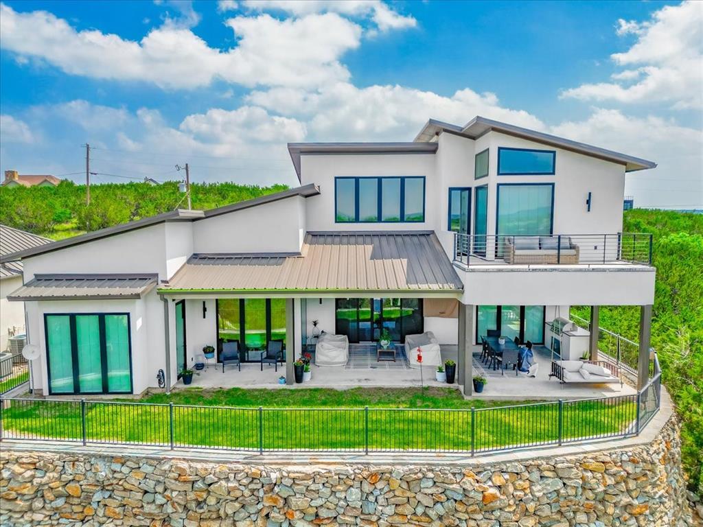 Perched within the sought-after Cliffs community at Possum Kingdom Lake, this striking 2023-built modern retreat delivers uninterrupted, panoramic lake views from nearly every room—and sits directly in front of the marina for unmatched convenience and a front-row seat to lake life. Designed to maximize its breathtaking setting, the home features soaring two-story windows in the living room that frame the water like art, filling the space with natural light. The all-white kitchen is both elegant and functional, highlighted by brushed brass fixtures, a dedicated coffee bar with built-in drink fridge, and seamless flow into the main living and dining areas—perfect for entertaining. A thoughtfully designed laundry room includes a sink and built-in desk space for added convenience. The primary suite offers a spa-like experience with a private sauna and a luxurious bath, while every bathroom in the home features deep soaking tubs for ultimate relaxation. Clean modern lines are complemented by a durable metal roof and native landscaping that blends beautifully with the natural surroundings. Outdoor living is equally impressive, with expansive patio and balcony spaces designed to take full advantage of the sweeping lake views. The covered patio includes a built-in gas grill, along with dedicated living and dining areas ideal for hosting or unwinding lakeside. As part of The Cliffs community, residents enjoy resort-style amenities including a championship golf course, marina, two pools, tennis courts, fitness center, restaurant, and gated security—offering a lifestyle that is as active or relaxed as you choose. A rare opportunity to own a nearly new, design-forward home in one of Possum Kingdom Lake’s premier neighborhoods.