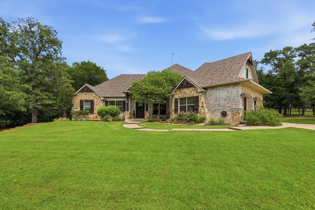 Stunning Cashion Custom Estate on 1.48 Acres! This exceptional single-story custom home combines timeless craftsmanship, luxurious finishes, and a peaceful country setting. Showcasing a striking brick and stone elevation, expansive front porch, and swing-entry two-car garage, this one-of-a-kind residence offers incredible curb appeal and thoughtfully designed living spaces throughout. Step inside to rich hardwood floors, soaring vaulted ceilings accented with exposed beams, and a grand floor-to-ceiling stone fireplace that anchors the spacious family room. Walls of windows flood the home with natural light while providing breathtaking views of the surrounding acreage. Carpet is being replaced. The charming, custom kitchen is filled with character and functionality, featuring a massive center island with gas cooktop, farmhouse sink, knotty alder cabinetry, unique pendant lighting, breakfast bar, and a convenient butler’s pantry. Every detail reflects the quality and craftsmanship that make this home truly special. Retreat to the expansive primary suite, complete with a private sitting area, vaulted beamed ceilings, and a luxurious spa-inspired bath. Generously sized secondary bedrooms are thoughtfully arranged in a split-bedroom floor plan, offering privacy and comfort for family and guests alike. Additional highlights include a large utility room with built-in cabinetry and sink, dedicated study, oversized garage with extra storage, and countless custom upgrades throughout. Outdoor living is equally impressive with a huge covered patio featuring a second stone fireplace, creating the perfect space for entertaining year-round. The beautifully maintained 1.48-acre homesite also includes a fenced dog run and an impressive 30' x 24' workshop with a finished office, ideal for hobbies, a home business, or additional workspace. A rare opportunity to own a truly custom estate offering exceptional style, functionality, and space both inside and out.