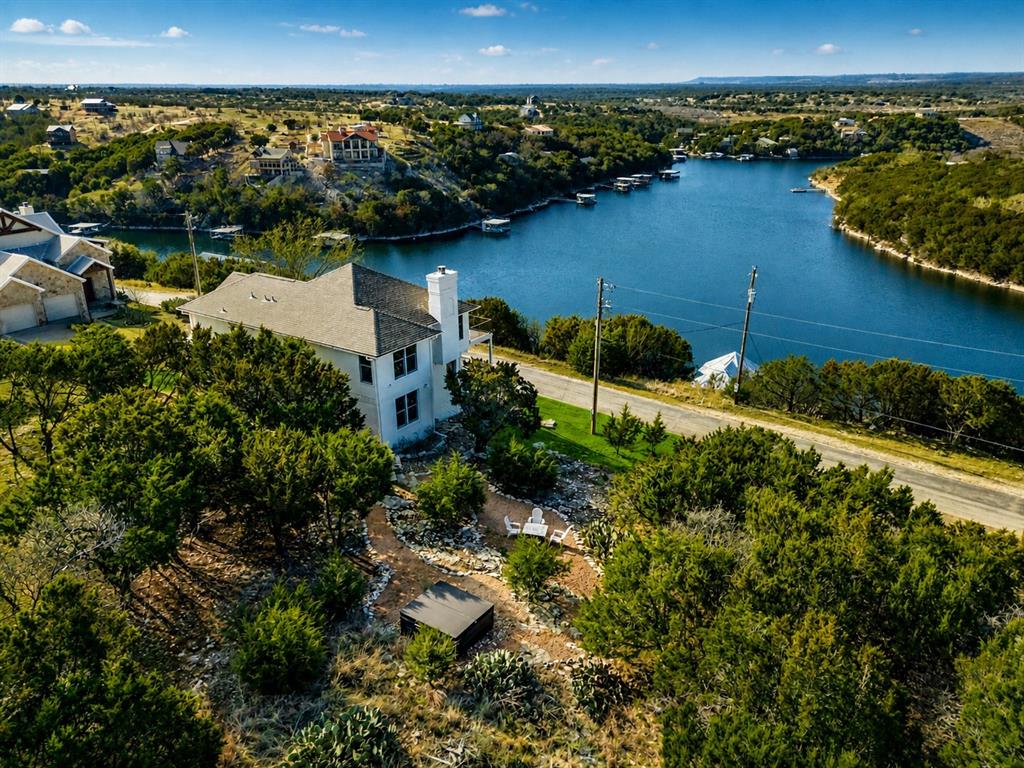 Exceptional two lot estate property with transferable boat slip, a truly rare find. Experience refined lake country living in this exquisitely updated residence located within the prestigious, gated Cliffs Resort on Possum Kingdom Lake. Offering stunning lake views and a hidden vantage point for the iconic Hells Gate 4th of July fireworks, this beautifully fully furnished home showcases an exceptional blend of luxury, comfort, and resort-style amenities, making it a rare turnkey opportunity ready to enjoy from day one. The thoughtfully designed floor plan features three bedrooms, two and a half bathrooms, and two spacious living areas. A large eat-in kitchen anchors the home, offering ample countertop space and an inviting layout perfect for gatherings, while expansive windows capture breathtaking lake vistas throughout the living spaces. Recent enhancements include fresh exterior and interior paint, rich hardwood flooring creating a seamless, upscale aesthetic throughout. The primary suite is a true retreat, highlighted by a completely remodeled, spa-inspired primary bathroom designed for relaxation and sophistication. Elegant statement chandeliers elevate both the front entry and dining room, adding architectural interest and a strong sense of arrival. Outdoor living is equally impressive. Fresh landscaping surrounds the home with curated bushes, exotic plants, and stone accents. A rare second lot expands the lifestyle possibilities, featuring a private spa-hot tub and a thoughtfully designed fire pit area with additional landscaping, perfect for entertaining or enjoying tranquil evenings under the Texas sky. For those seeking future expansion, the property includes two complete sets of architectural plans for a potential home addition, complete with multiple renderings showcasing pool and backyard concepts, an exceptional opportunity to further customize an already impressive residence.