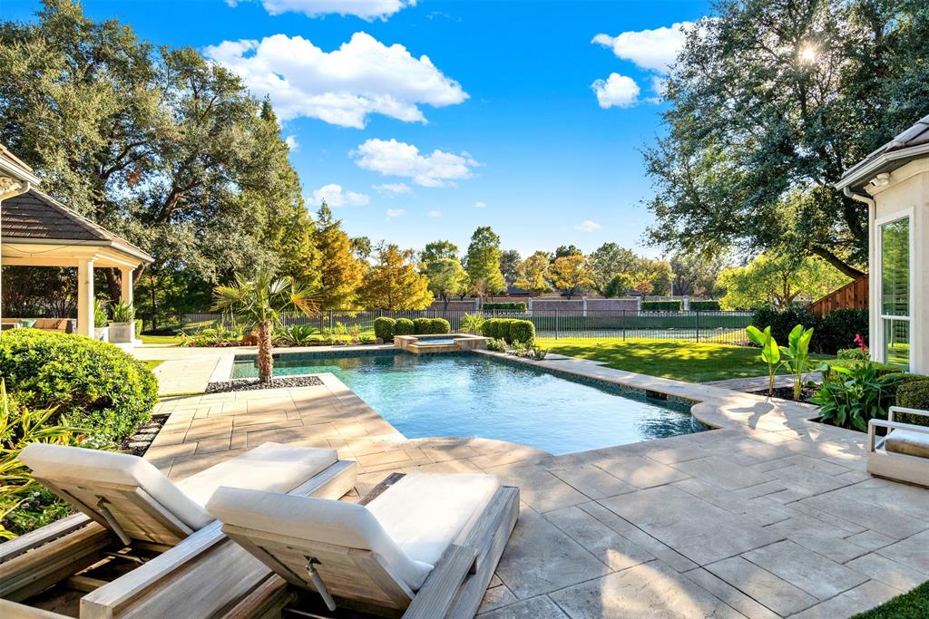Nestled in the serene embrace of Willow Bend Polo Estates, this beautifully updated custom home sits on nearly half an acre, offering a private retreat with a lush greenbelt and tranquil lake as your backdrop. Imagine spending your days unwinding in your very own resort-style backyard oasis, complete with a refreshing pool and spa, a charming 5-hole putting green, and a spacious cabana equipped with a grill and surround sound, all while soaking in the peaceful views. Inside, every room has been lovingly updated, ensuring no detail has been overlooked. As you step through the foyer, you're greeted by the living room's stunning tile fireplace, soaring 20-foot ceiling, and a breathtaking wall of windows that frame the pool, backyard, and greenbelt. The gourmet kitchen is a chef's dream, featuring a Wolf 6-burner gas cooktop with griddle, Wolf double ovens, quartz countertops, a built-in Sub-Zero fridge and freezer, and a generous walk-in pantry, along with two additional storage closets. The breakfast nook offers more stunning views and opens to a cozy family room with a wet bar, ice maker, ceiling beams, marble tile fireplace, and a custom-mounted TV with indoor and outdoor surround sound. The primary bedroom is a sanctuary you may never want to leave, with its own fireplace, bay windows overlooking the greenbelt and lake, hardwood floors, and a luxurious updated bath with quartz counters, double vanities, a free-standing tub, and a custom closet. A second bedroom is conveniently located off the kitchen for added privacy. The back staircase leads to a spacious game room and three additional bedrooms with two full baths. Your 3-car garage features an epoxy floor and an electric vehicle charging outlet, all just minutes away from DNT, 190, Stonebriar Mall, Legacy West, and so much more.